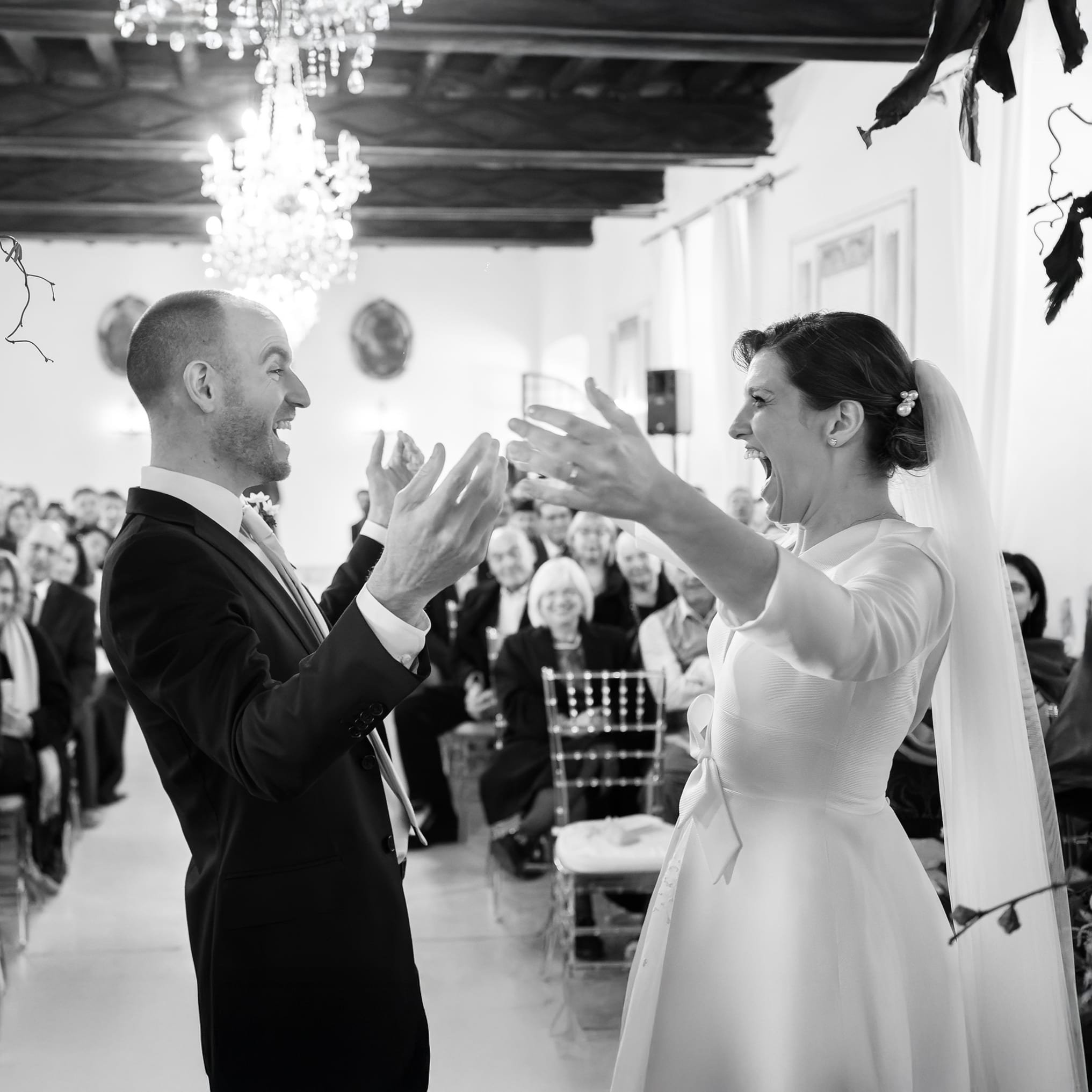 Bride and groom celebrating during wedding ceremony, surrounded by guests, in an elegant indoor venue.