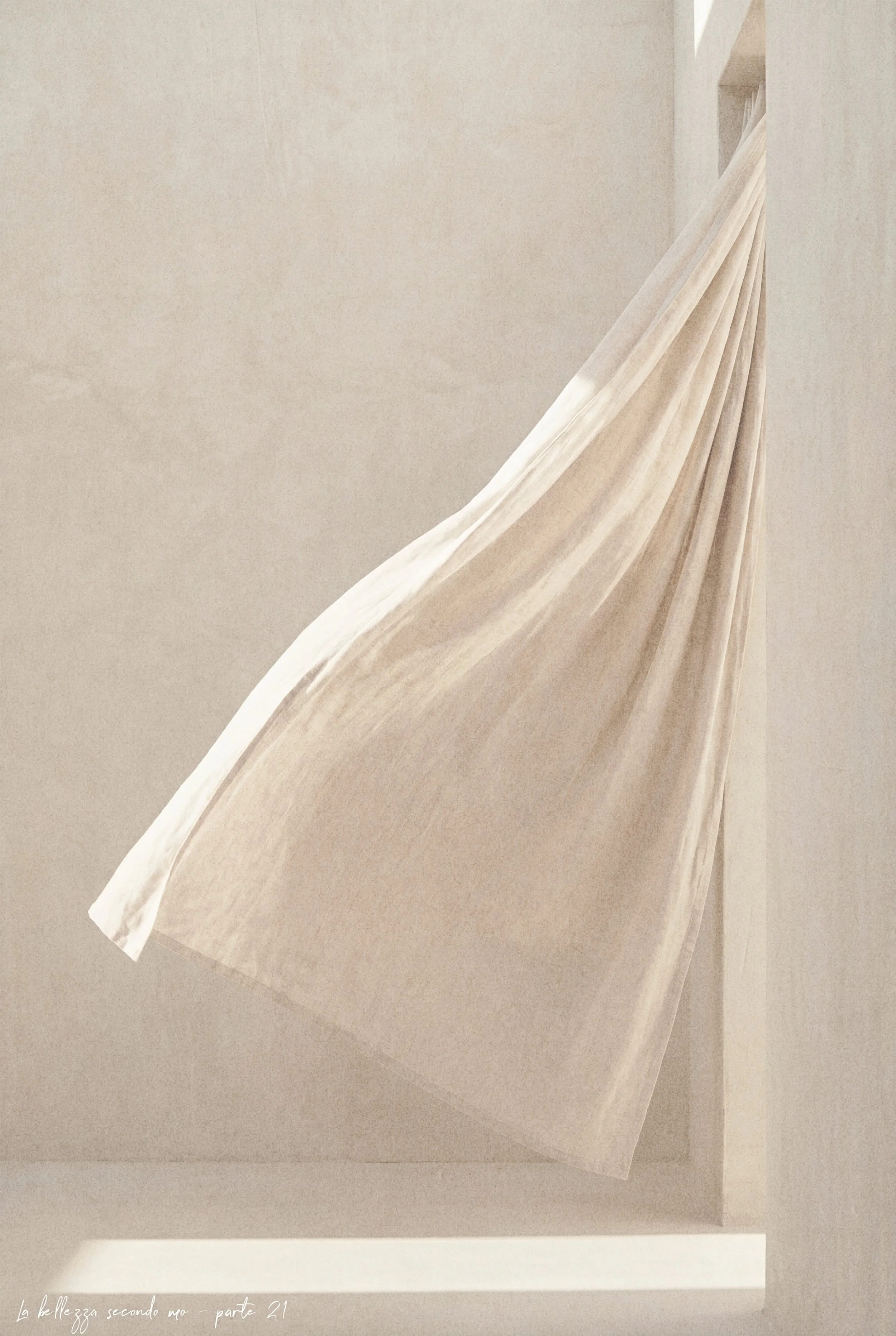 A beige curtain hanging in a minimalist room with neutral-colored walls.