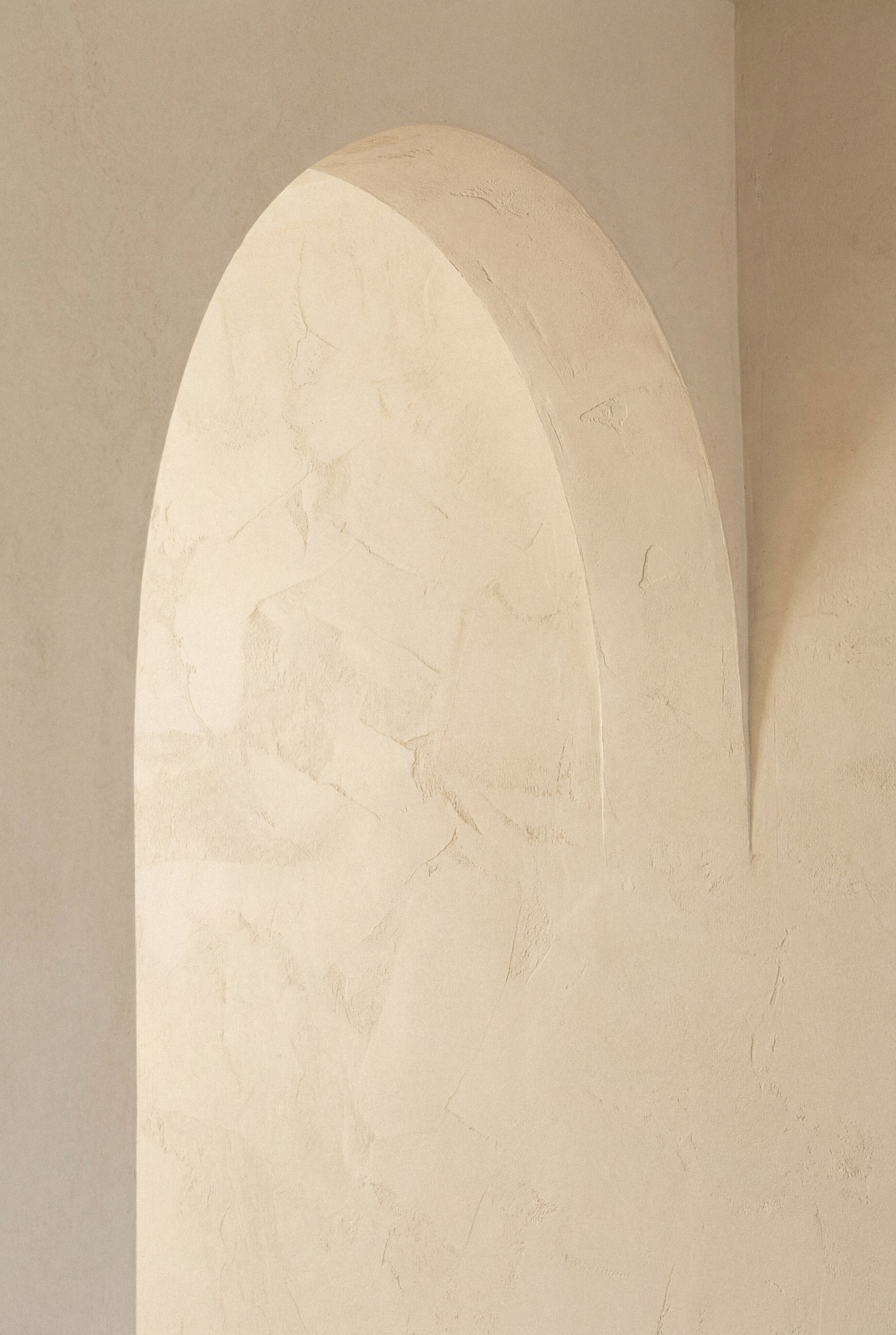 A textured white wall with an arched cutout or niche, creating a shadowed recess in the wall.