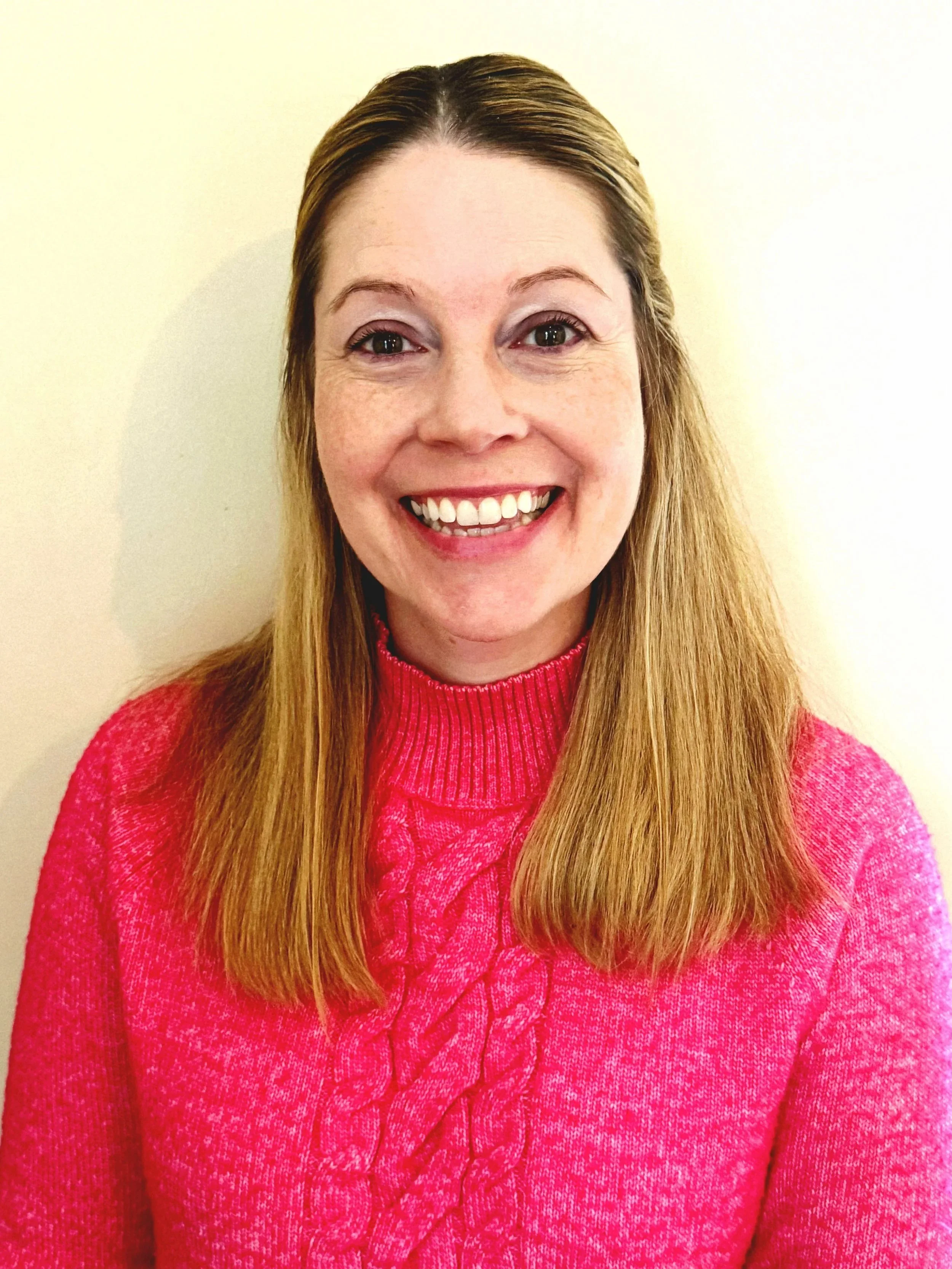 Woman in teal top smiling in front of a brick wall.