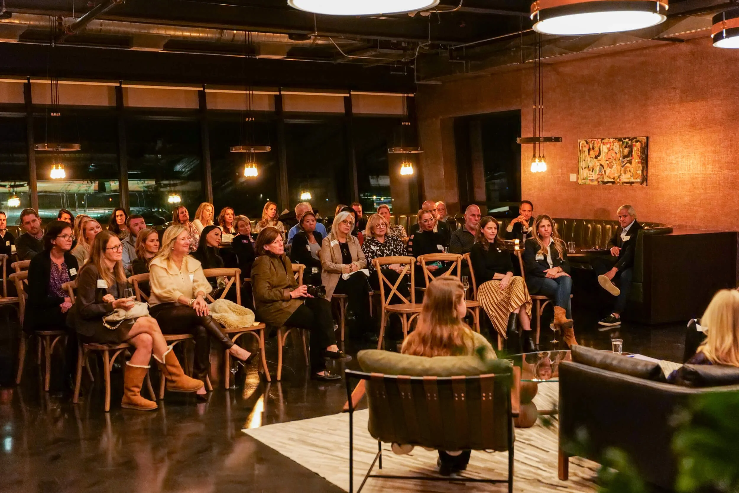 Group of people seated in a stylish room attending a presentation or event.