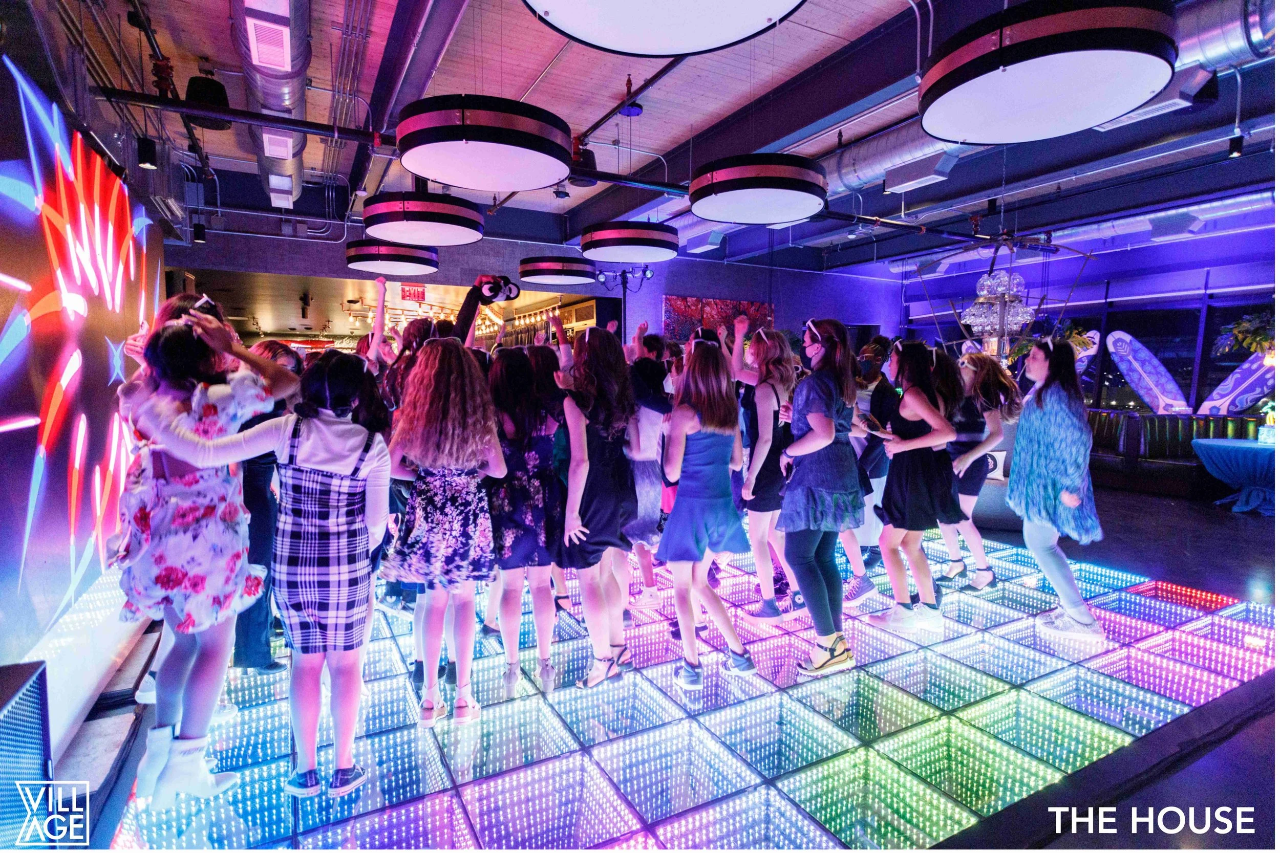 A group of women dancing on a colorful LED dance floor at a party or nightclub, with vibrant lighting and modern decor.