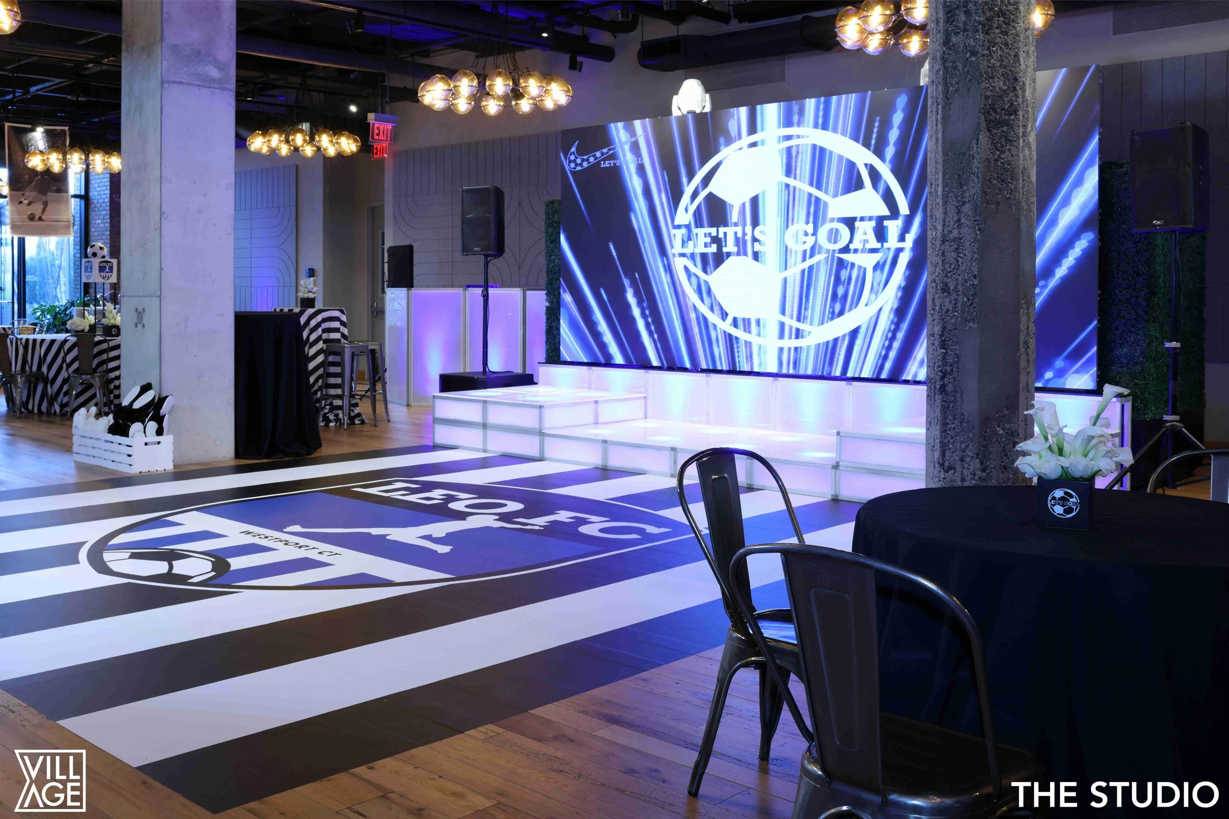 Indoor event space decorated with Southwest FC soccer theme, featuring a large LED screen displaying the text "LET'S GOAL" with soccer graphics, a black table with flowers, and a striped floor resembling a soccer field with the team logo.