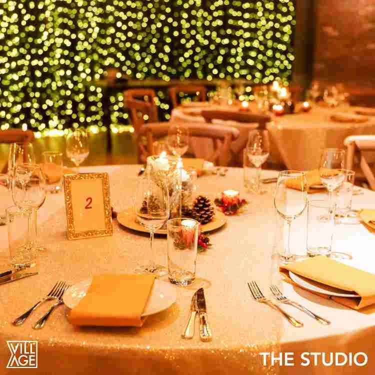 Elegant banquet table decorated for a holiday event with candles, pinecones, and Christmas ornaments, illuminated by string lights in the background.