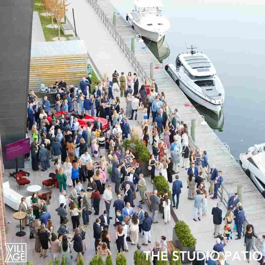 A large group of people gathered on a marina dock, with yachts moored nearby, attending an outdoor event on a cloudy day.