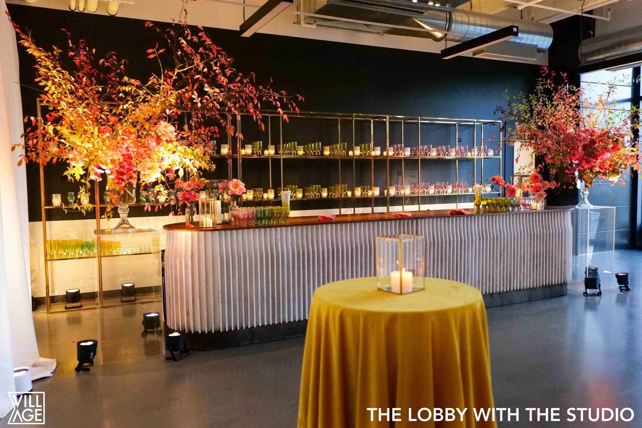 Elegant event lobby featuring a bar with floral arrangements and candles, with warm lighting and modern decor.