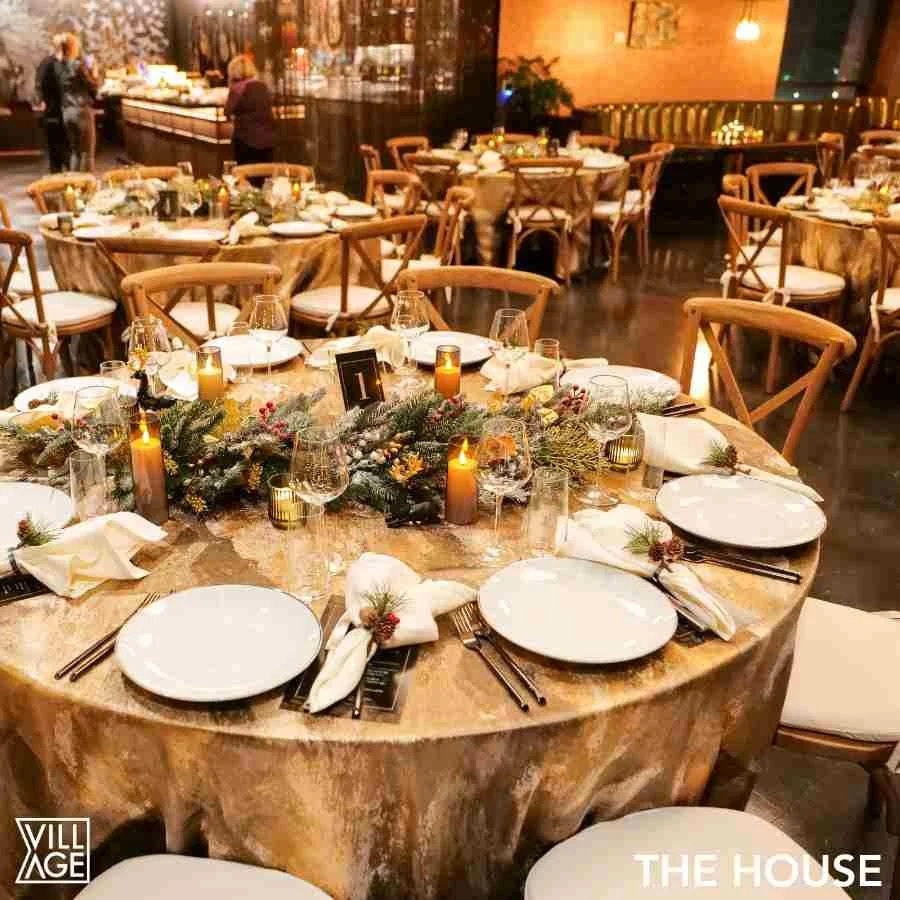 A round banquet table set for a holiday dinner with candles, greenery, and decorated napkins in a warmly lit restaurant.