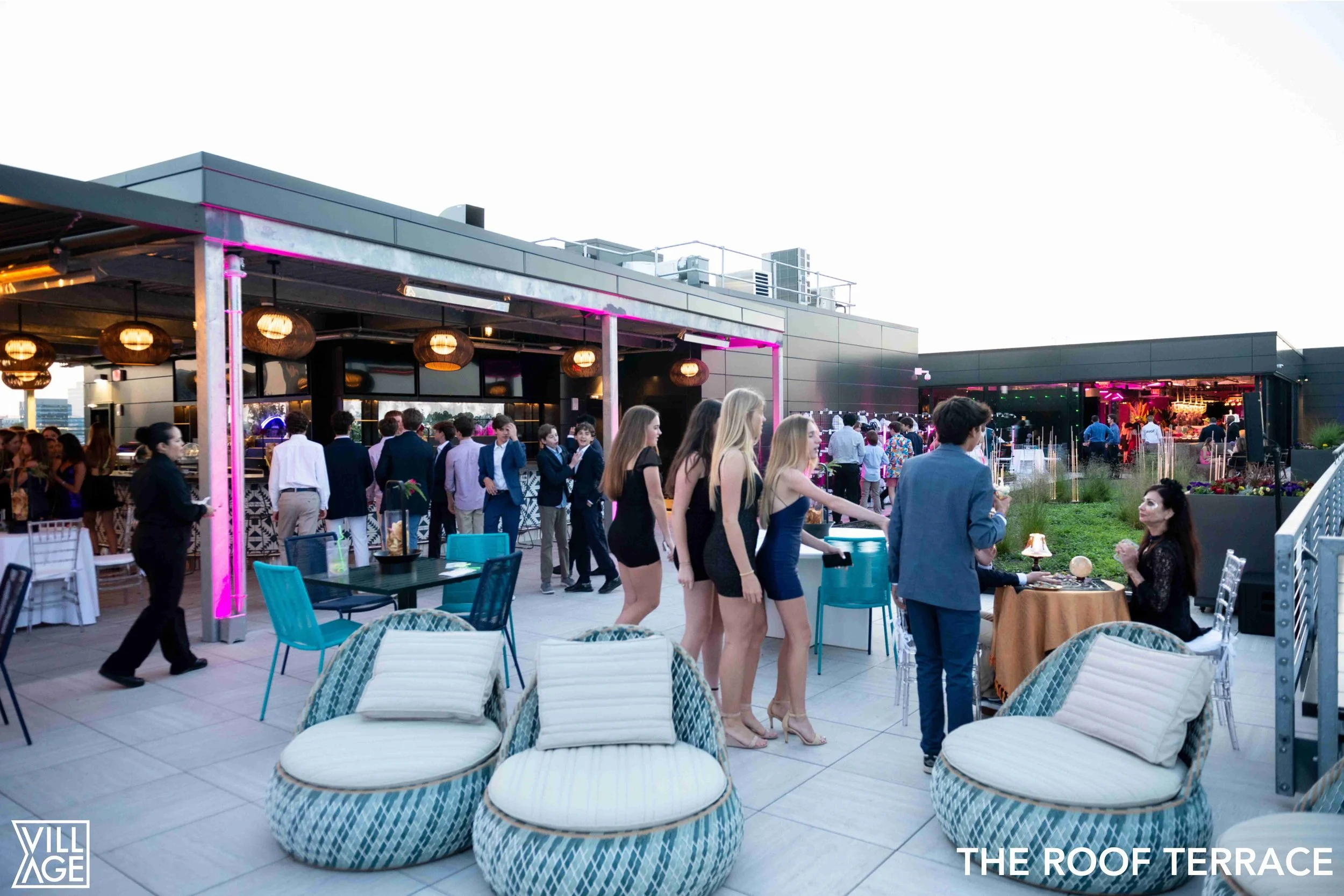 People socializing on an outdoor rooftop terrace with modern furniture and bar area at sunset.