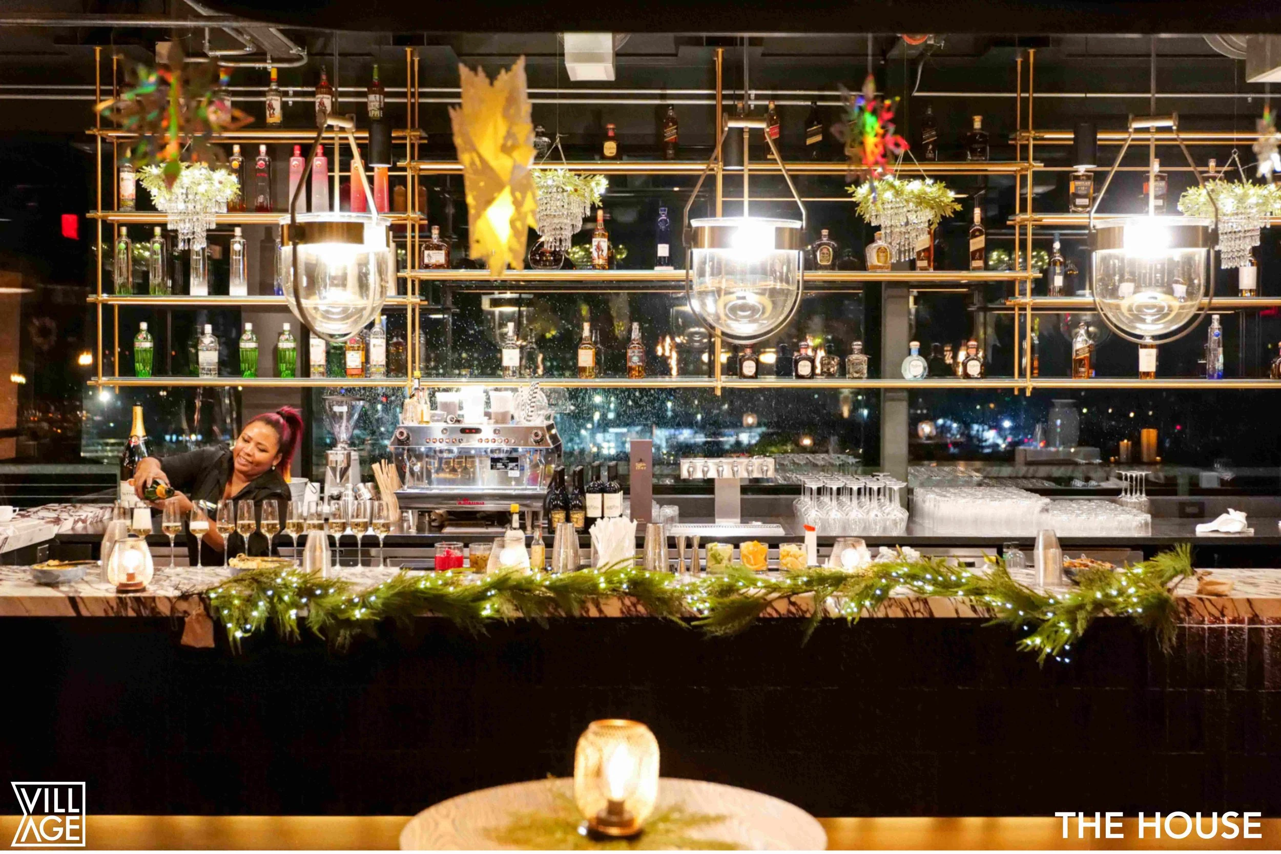 A bartender preparing drinks behind a festive bar with Christmas decorations, garlands, and lights at night in a modern restaurant or bar.