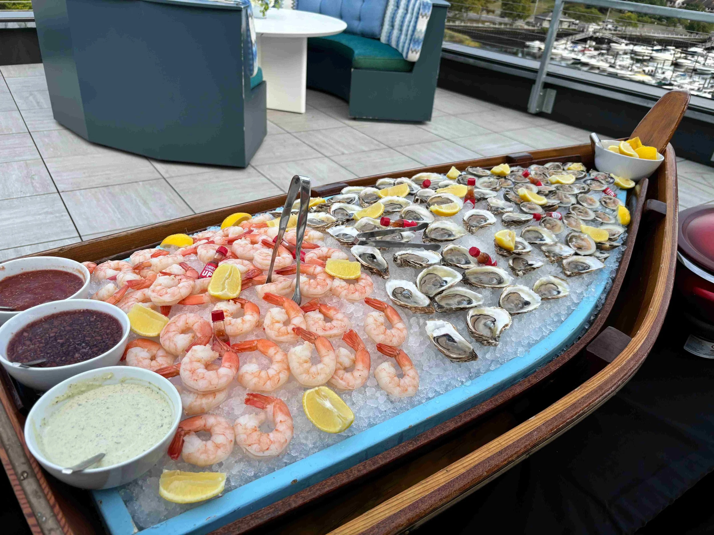 Seafood buffet with shrimp, oysters, lemon wedges, and dipping sauces on a boat deck