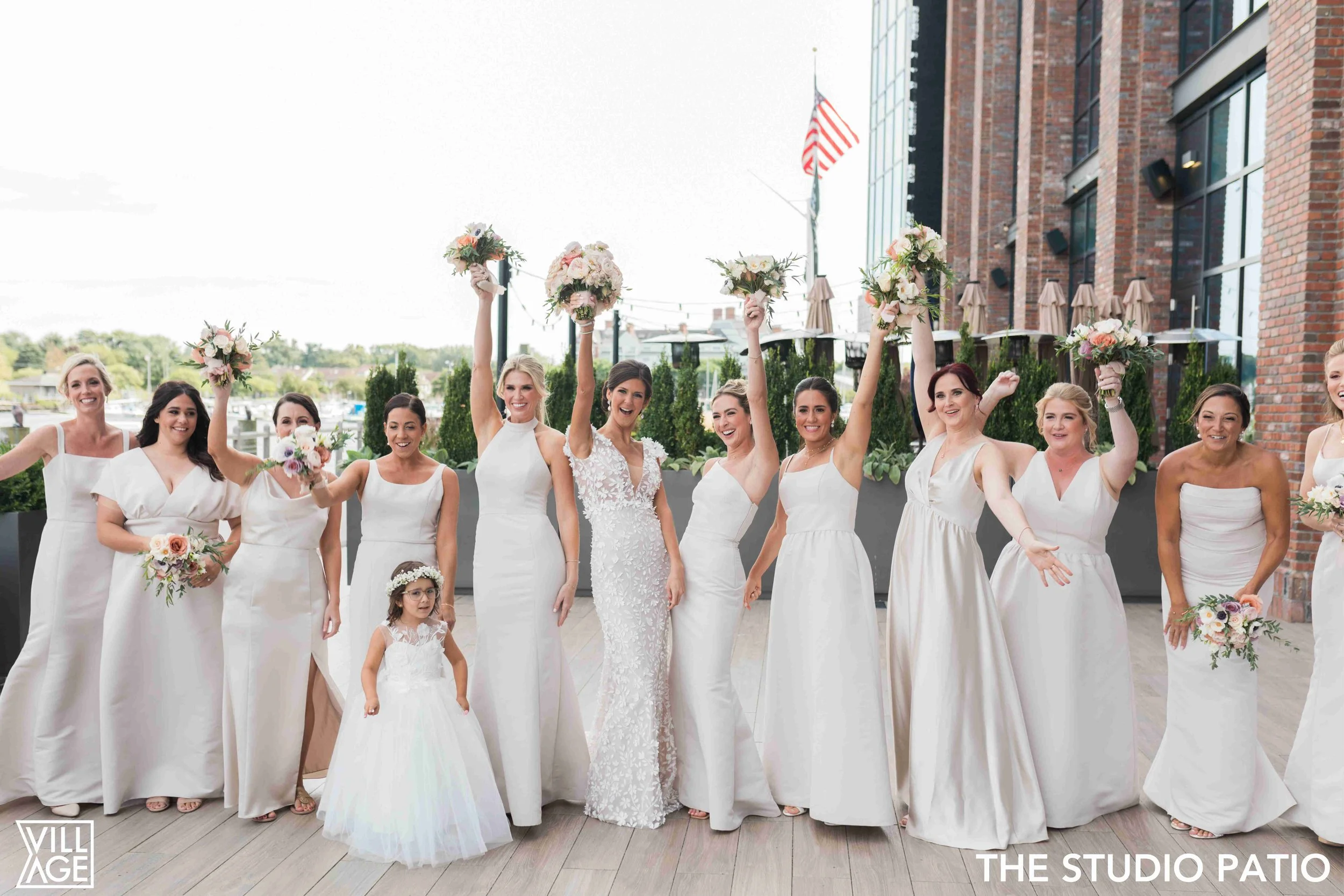 Bride and bridesmaids celebrating with bouquets on outdoor patio at a wedding.