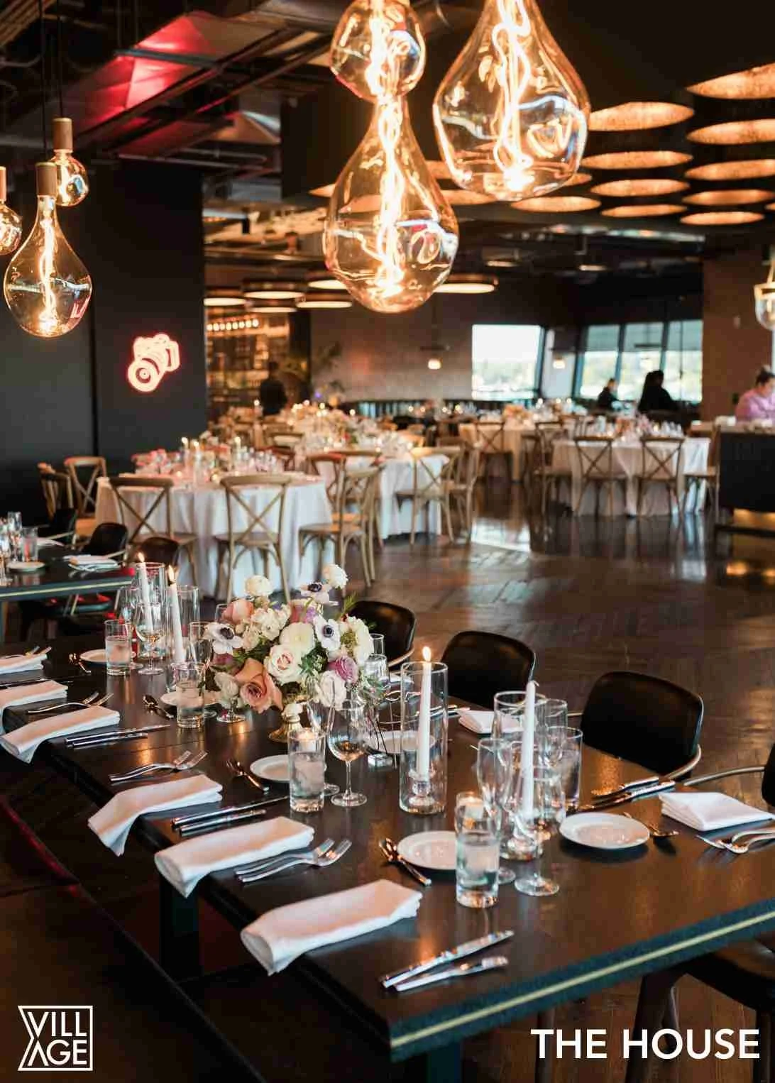 Elegant restaurant dining area with decorated tables, large glass pendant lights, and floral centerpieces.
