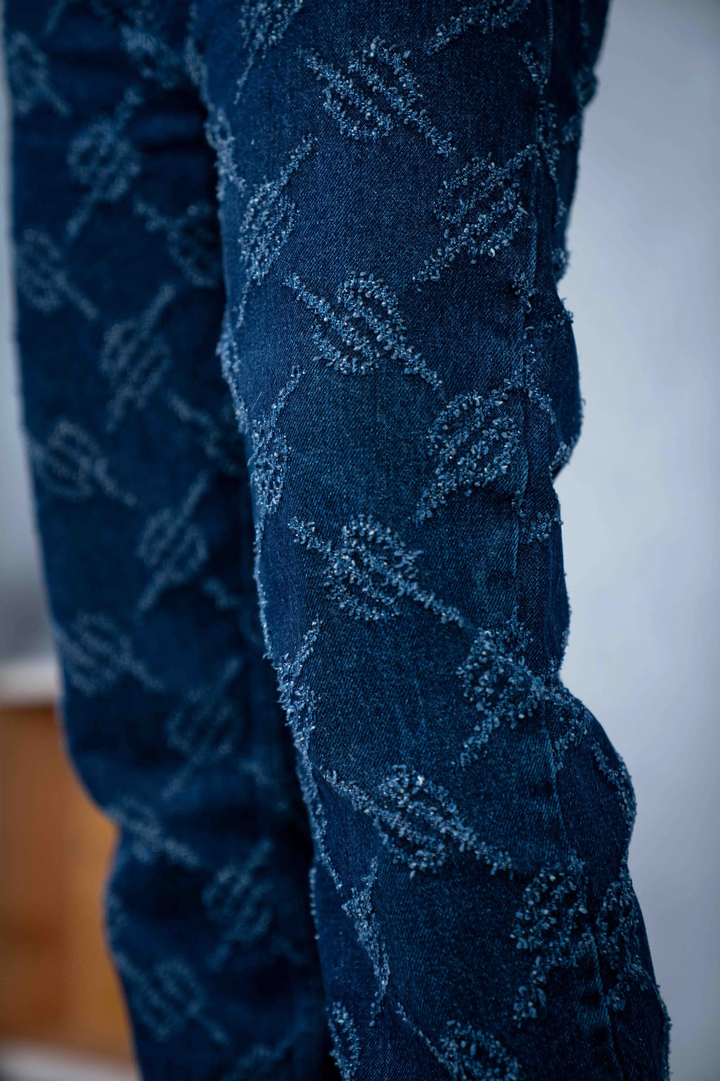 Close-up of dark denim jeans with an embroidered pattern of trees.