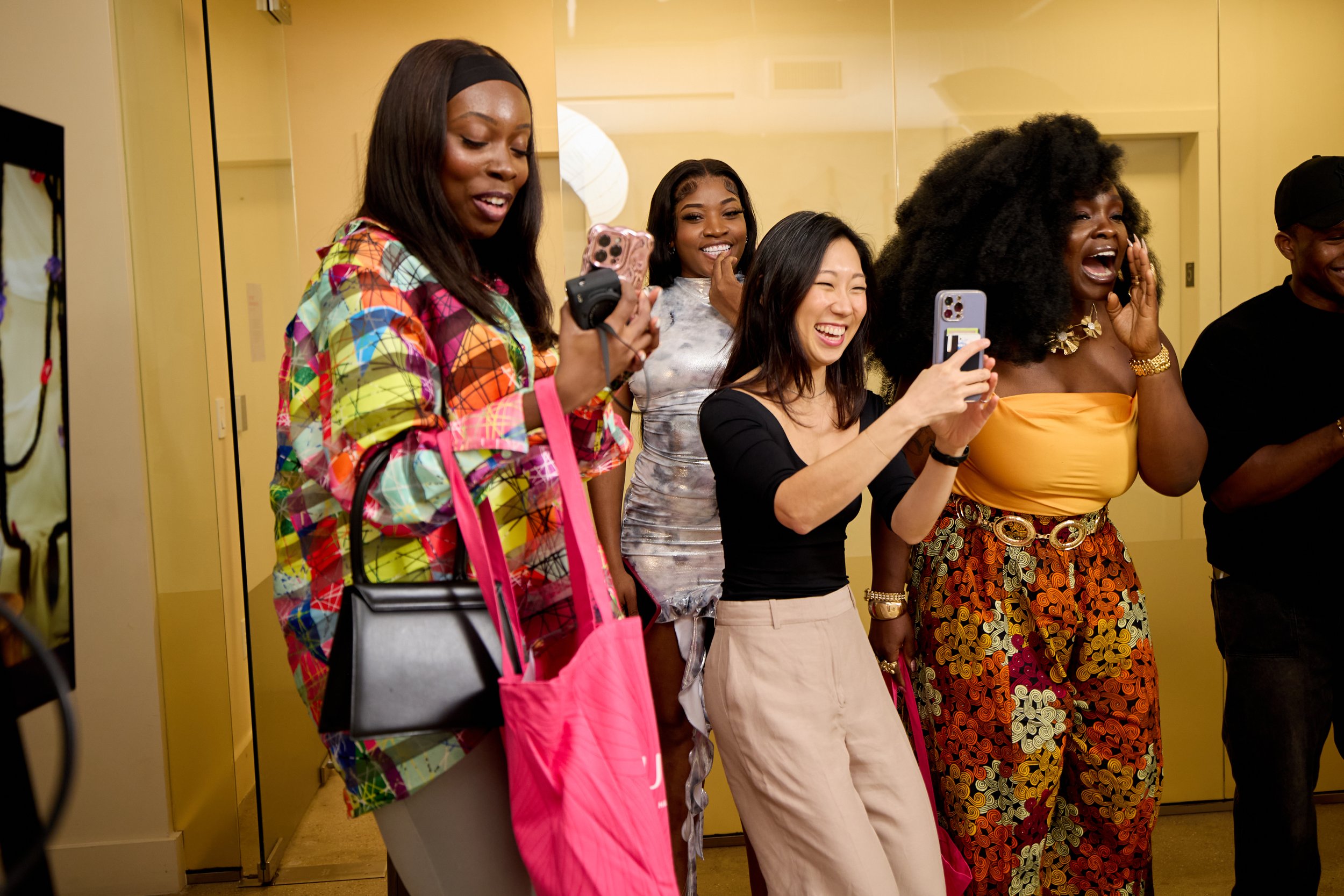 Group of women laughing and taking photos together in an indoor setting.