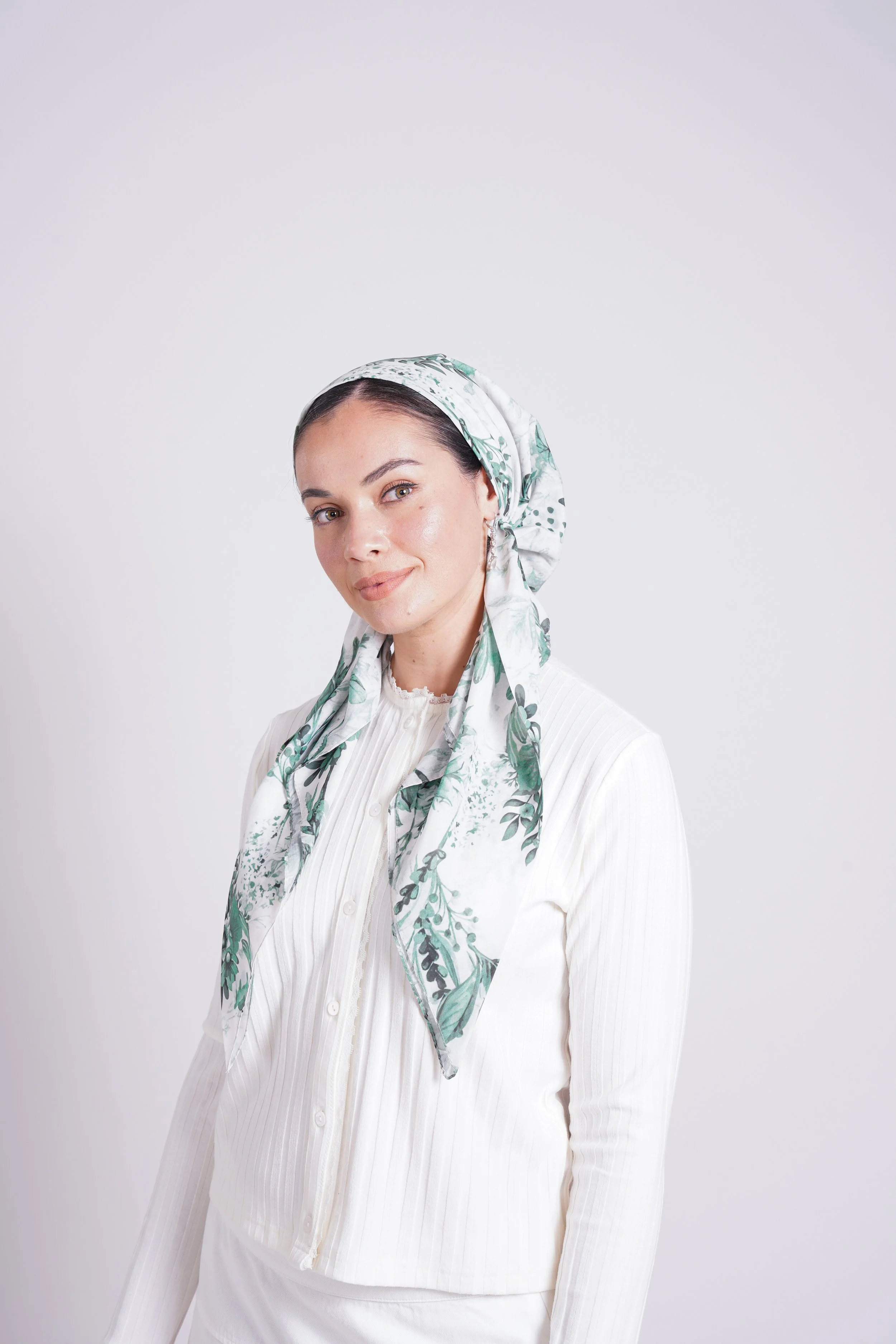 Portrait of a woman wearing a white blouse and a floral headscarf, smiling softly against a plain white background.