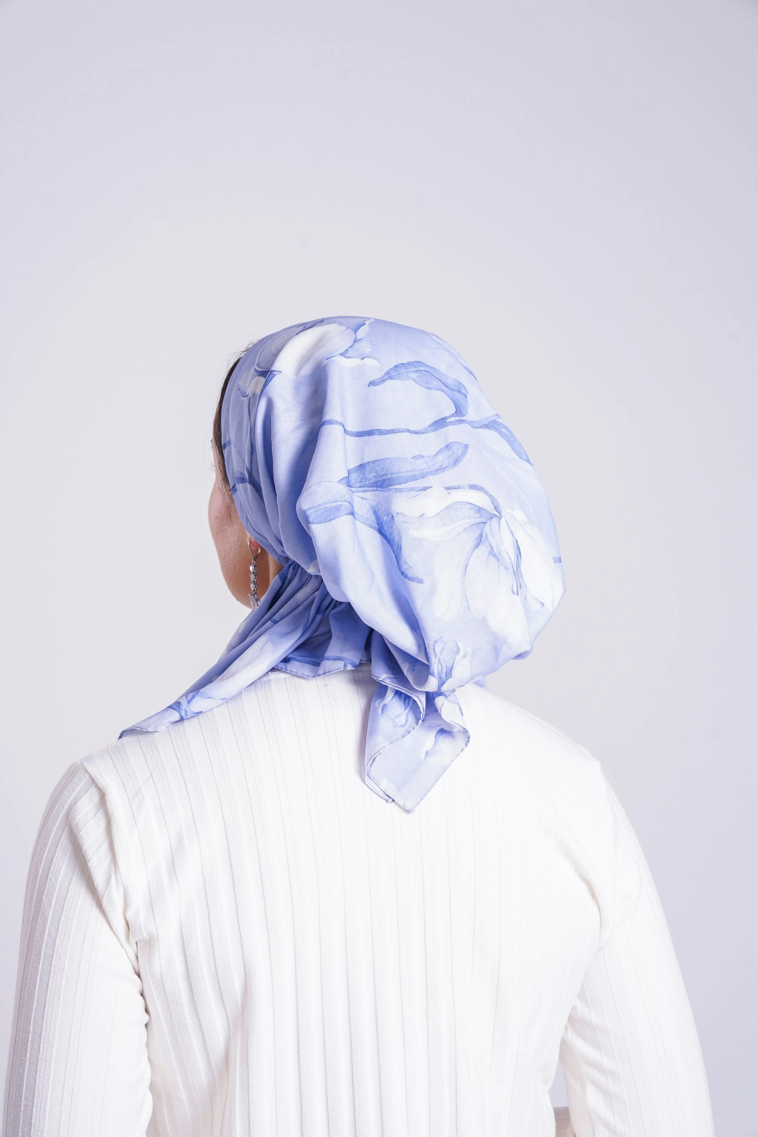 A woman with earrings wearing a light-colored, vertically striped shirt and a blue floral headscarf.