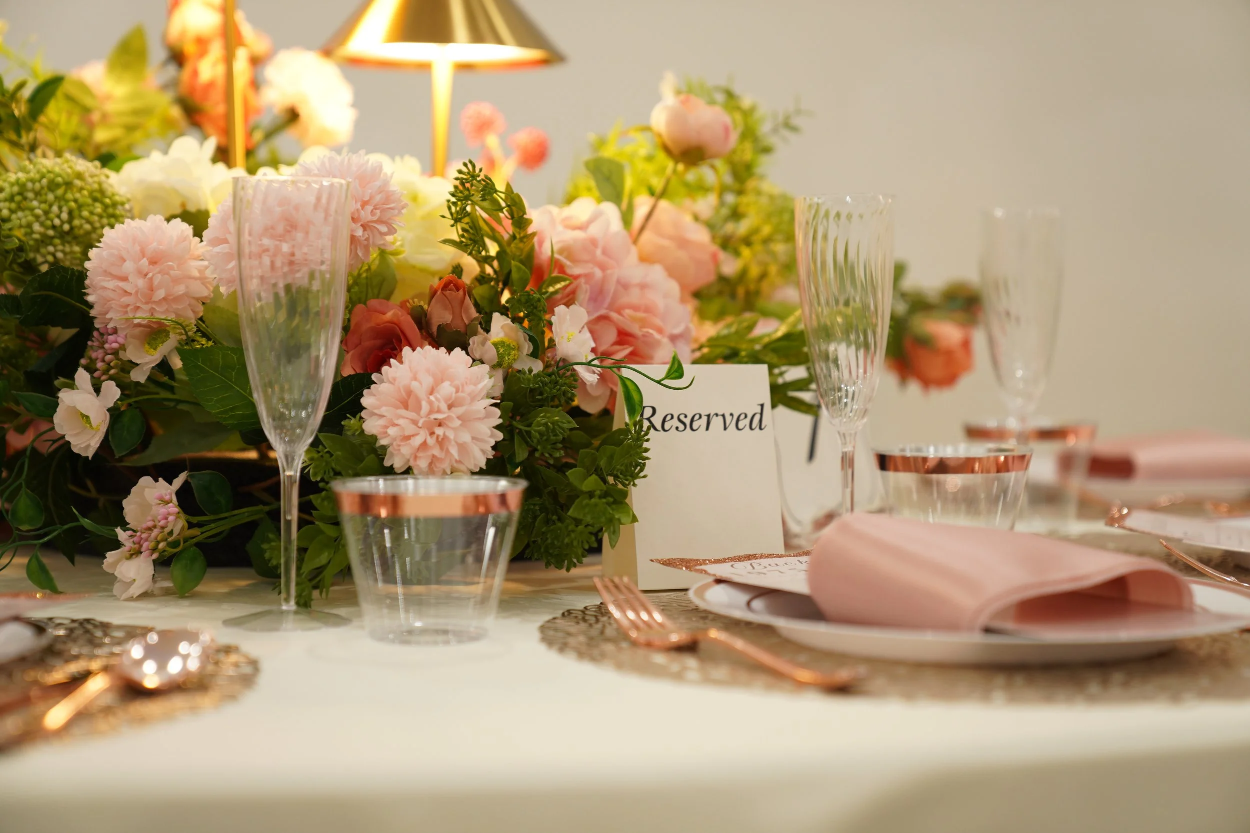 Elegant table setting with a floral centerpiece, champagne glasses, pink napkins, and reserved sign on a white tablecloth for a formal event or wedding