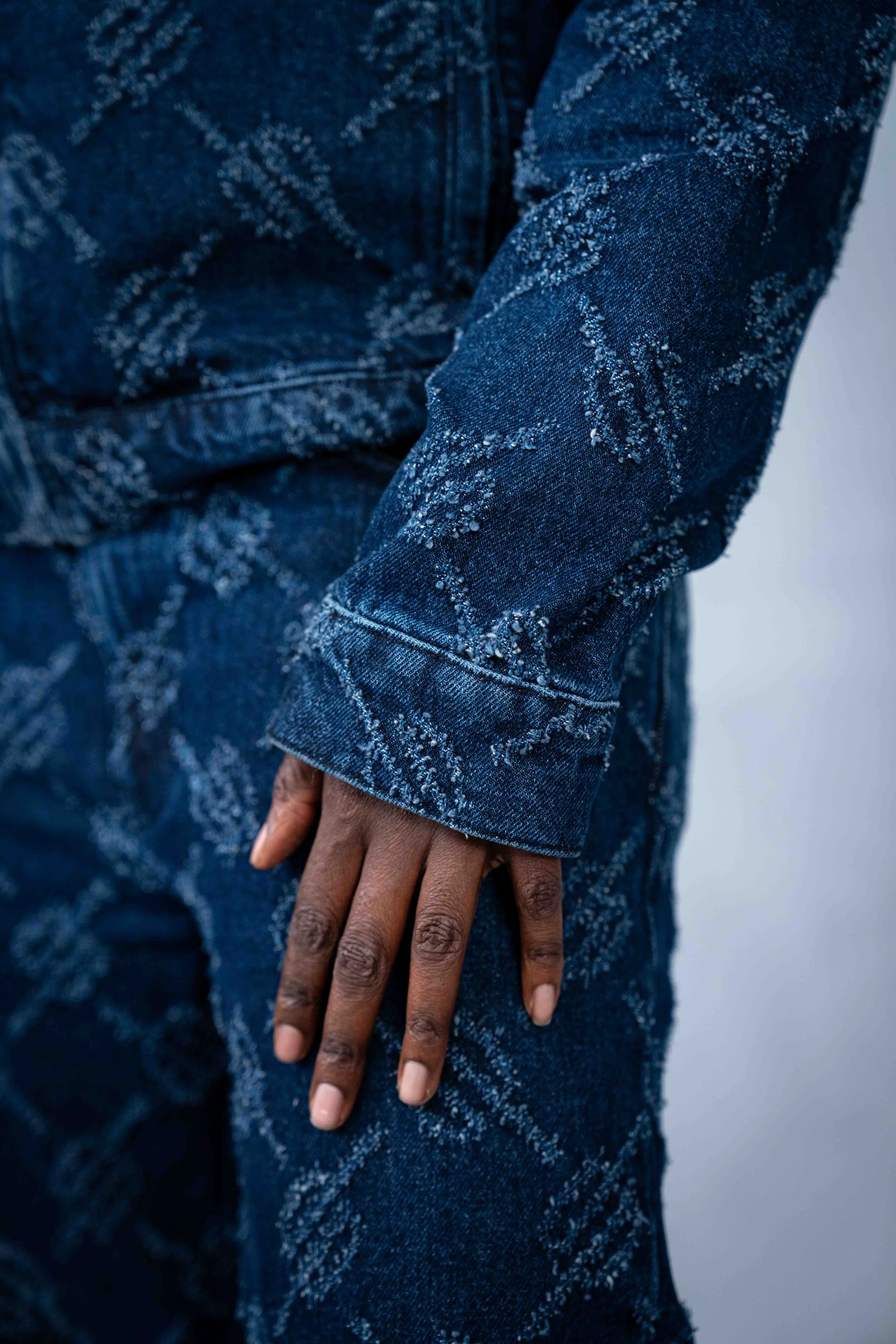 Close-up of a person wearing a dark blue patterned denim outfit, with their hand resting on their thigh.