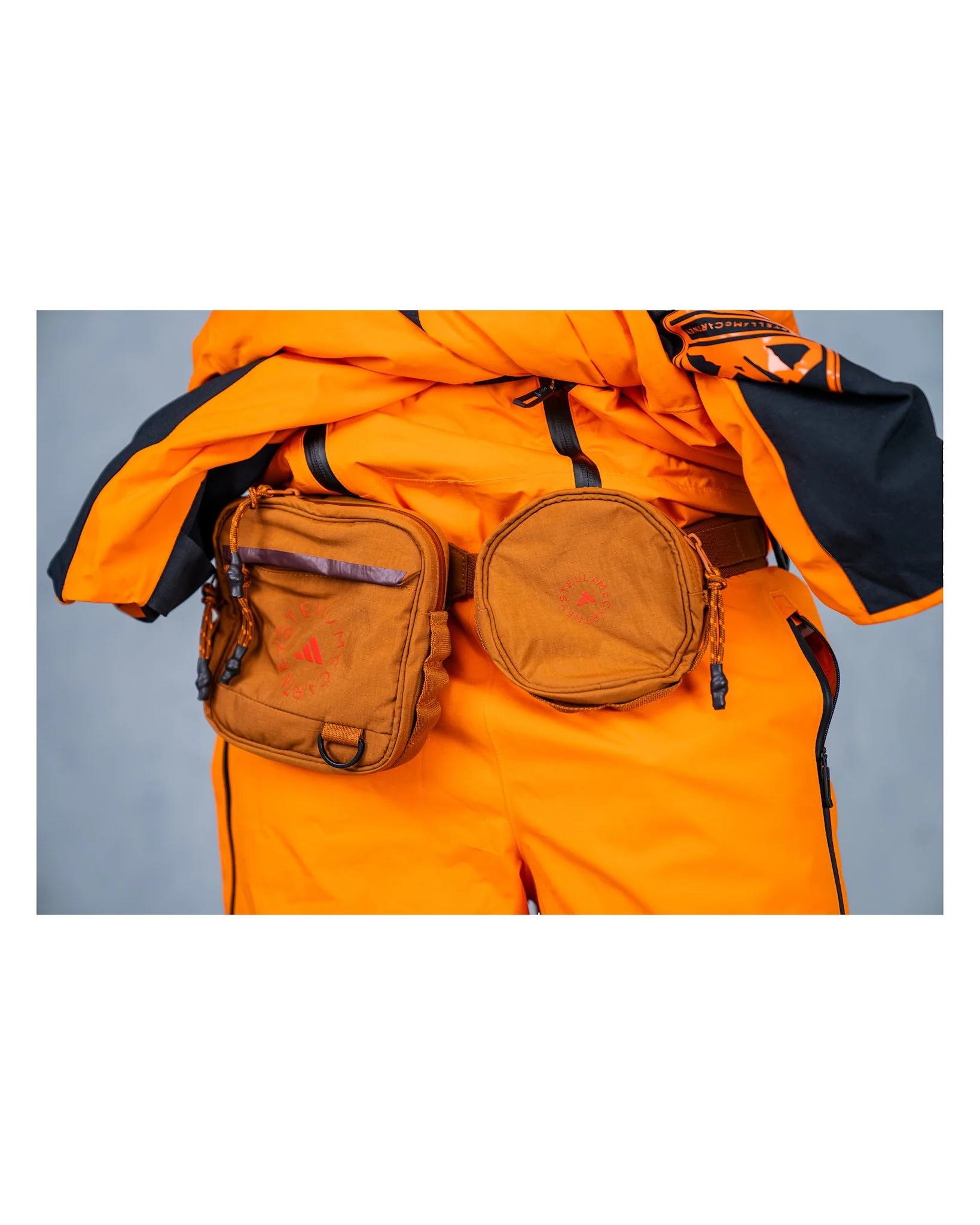 Person wearing bright orange outdoor gear with two brown shoulder bags attached to the waist