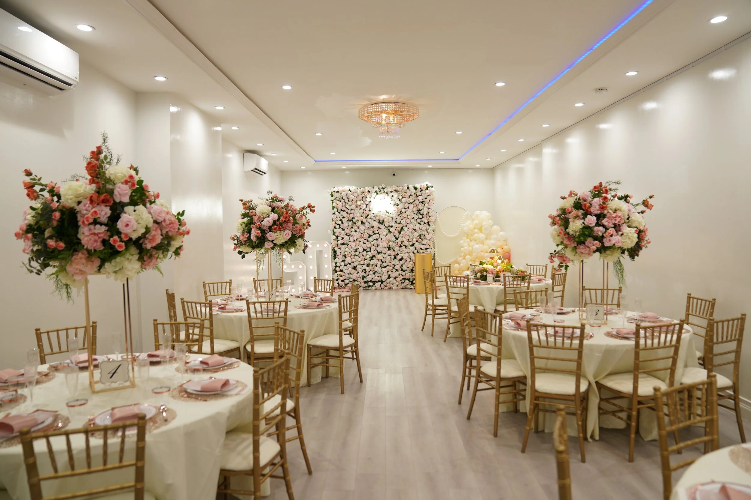 Elegant banquet hall decorated with pink and white flowers, gold chairs, and white tablecloths for a wedding reception.