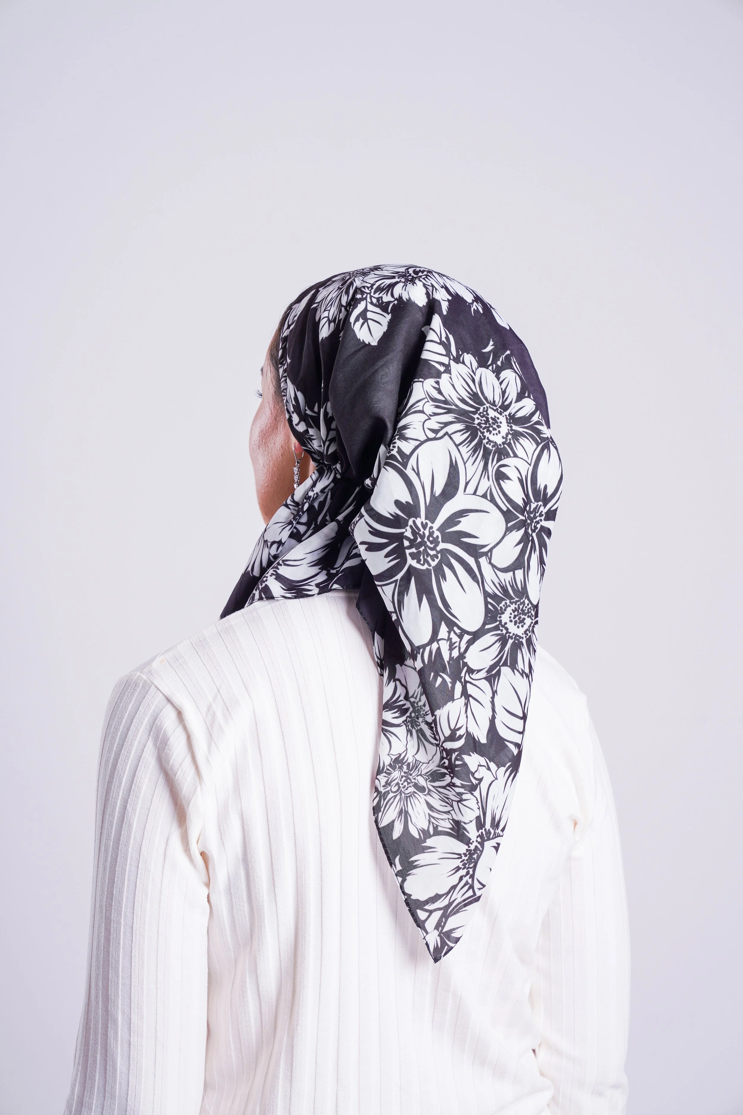 Woman wearing a black and white floral patterned headscarf and a white pinstriped shirt, facing away from the camera.