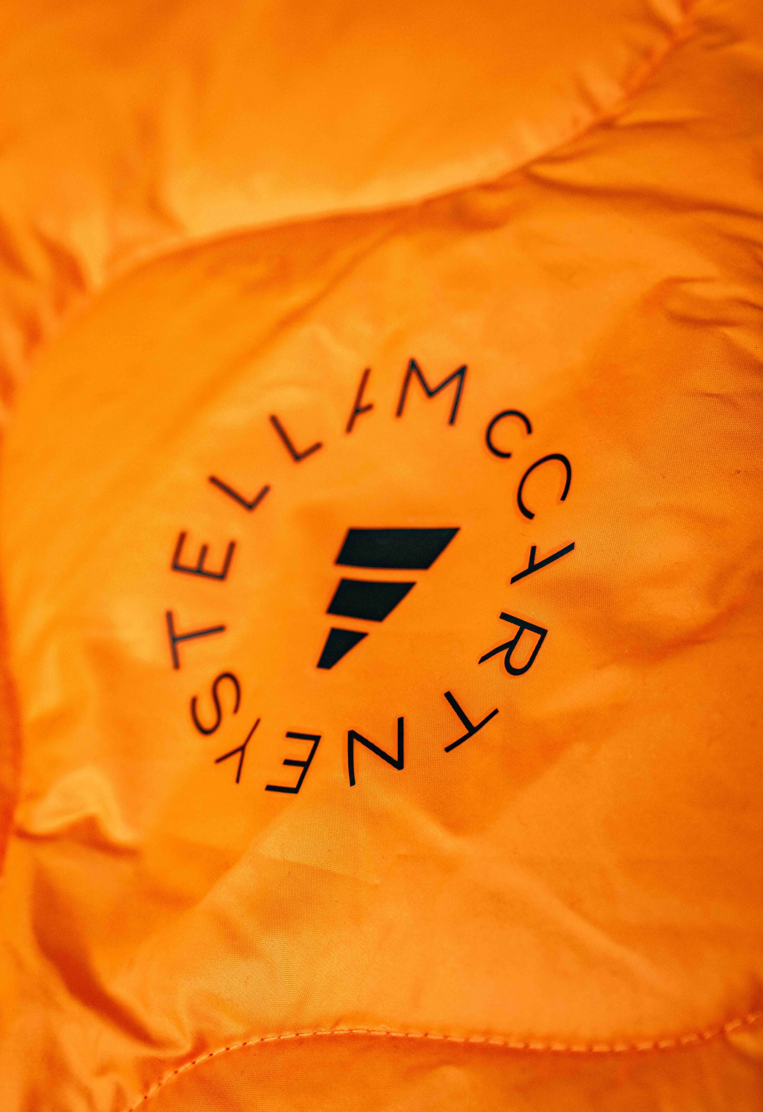 Close-up of orange fabric with black logo that reads 'TRAVEL COMFORT MYSELF' arranged in a circle around a stylized black feather.