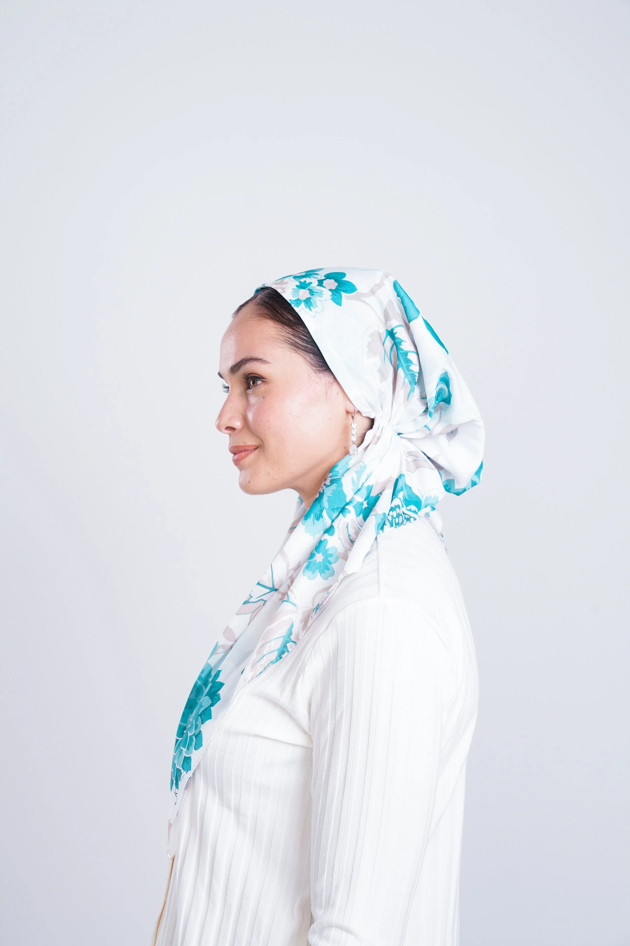 Profile view of a woman wearing a white blouse and a floral headscarf with blue and white patterns.