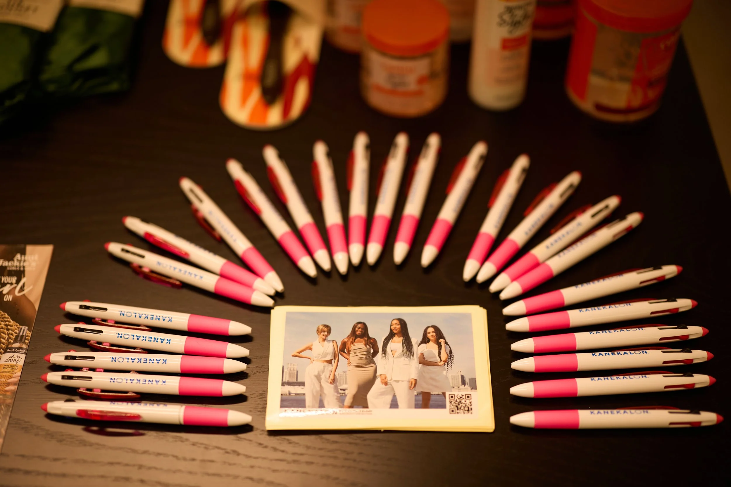 A table with pink and white pens arranged in a semi-circle around a photo of four women standing outdoors with city buildings in the background.