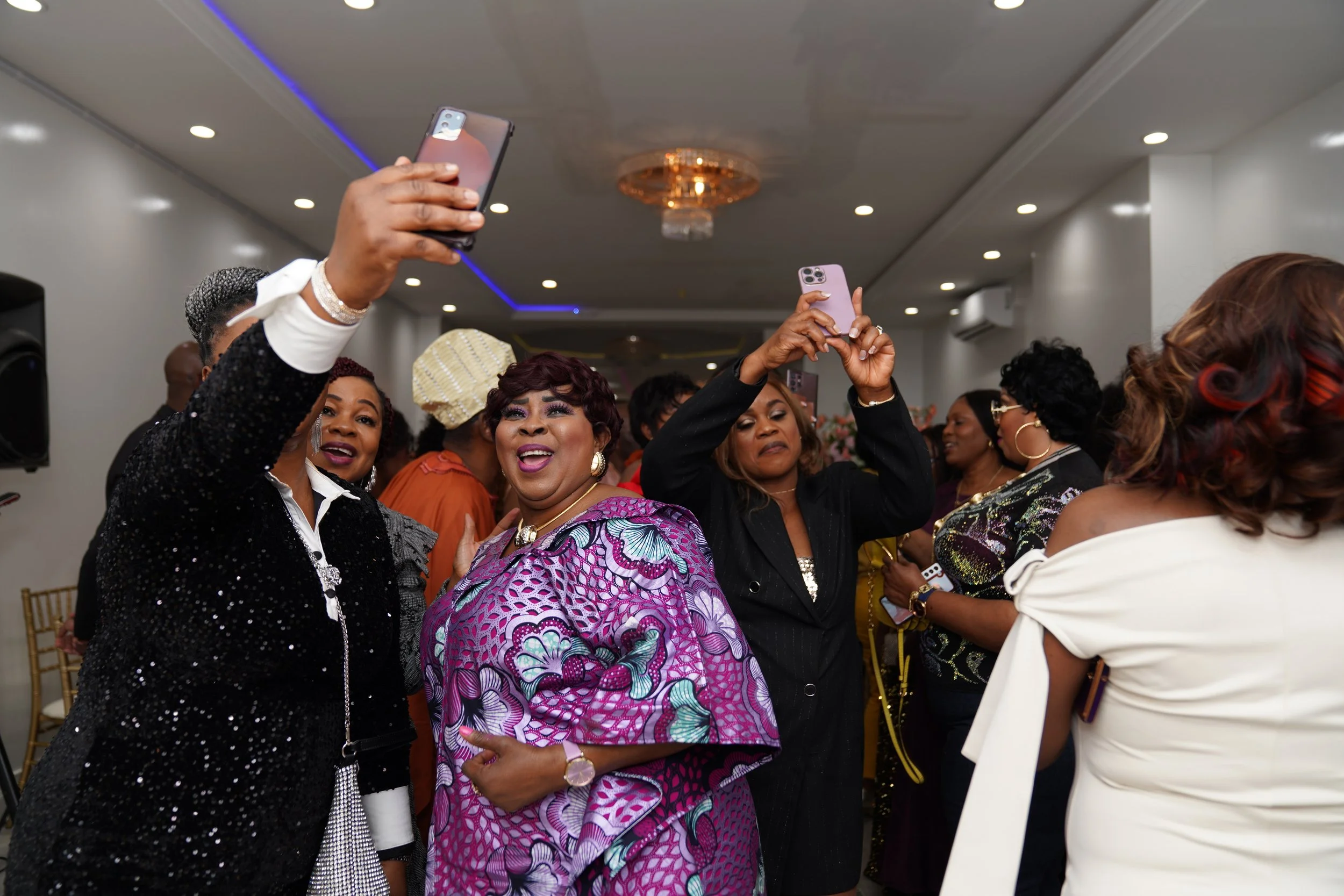 Women at a celebration taking photos with phones in a decorated indoor setting.
