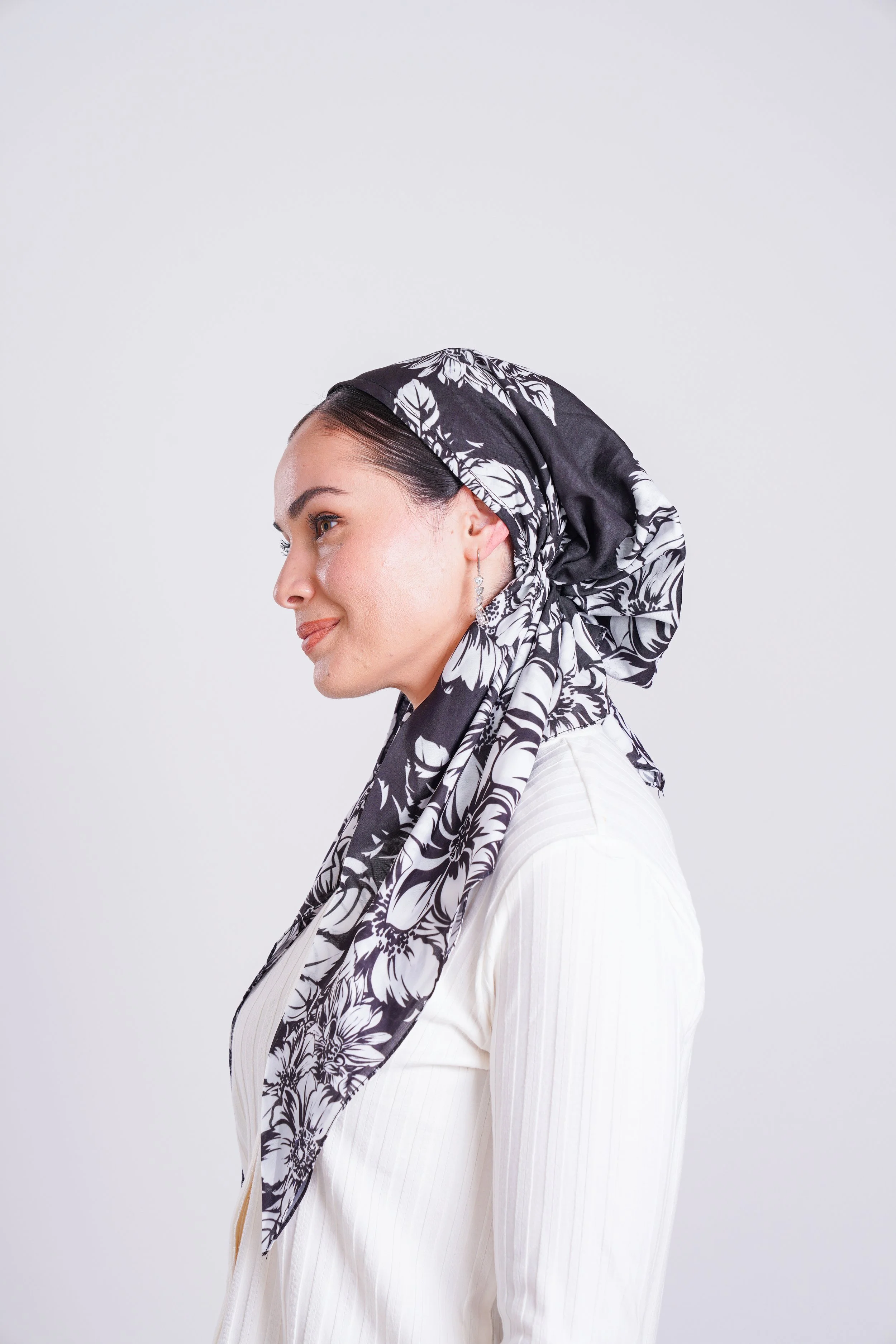 A woman in profile wearing a black and white floral headscarf and white shirt.