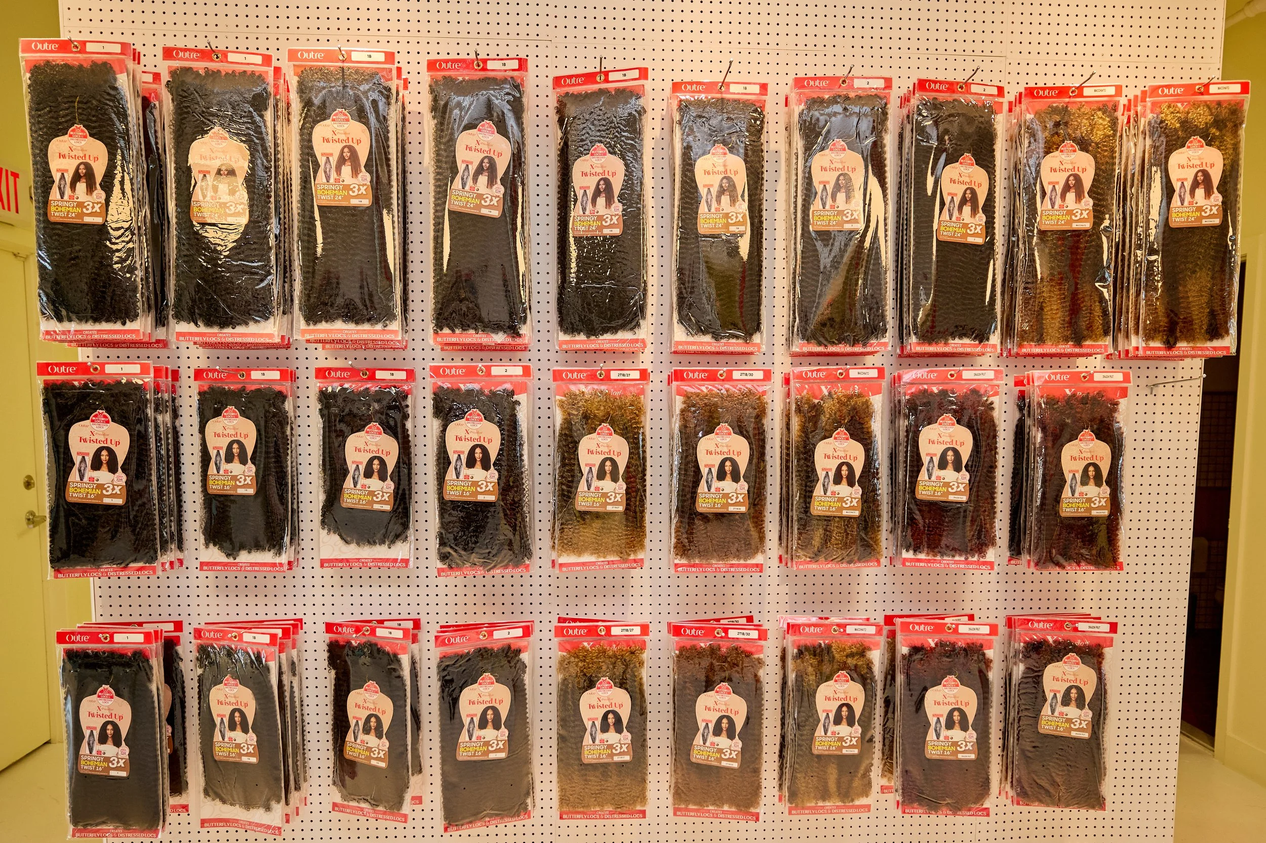 Display of hair extensions or wigs in black, brown, and blonde colors hanging on a pegboard in a store.