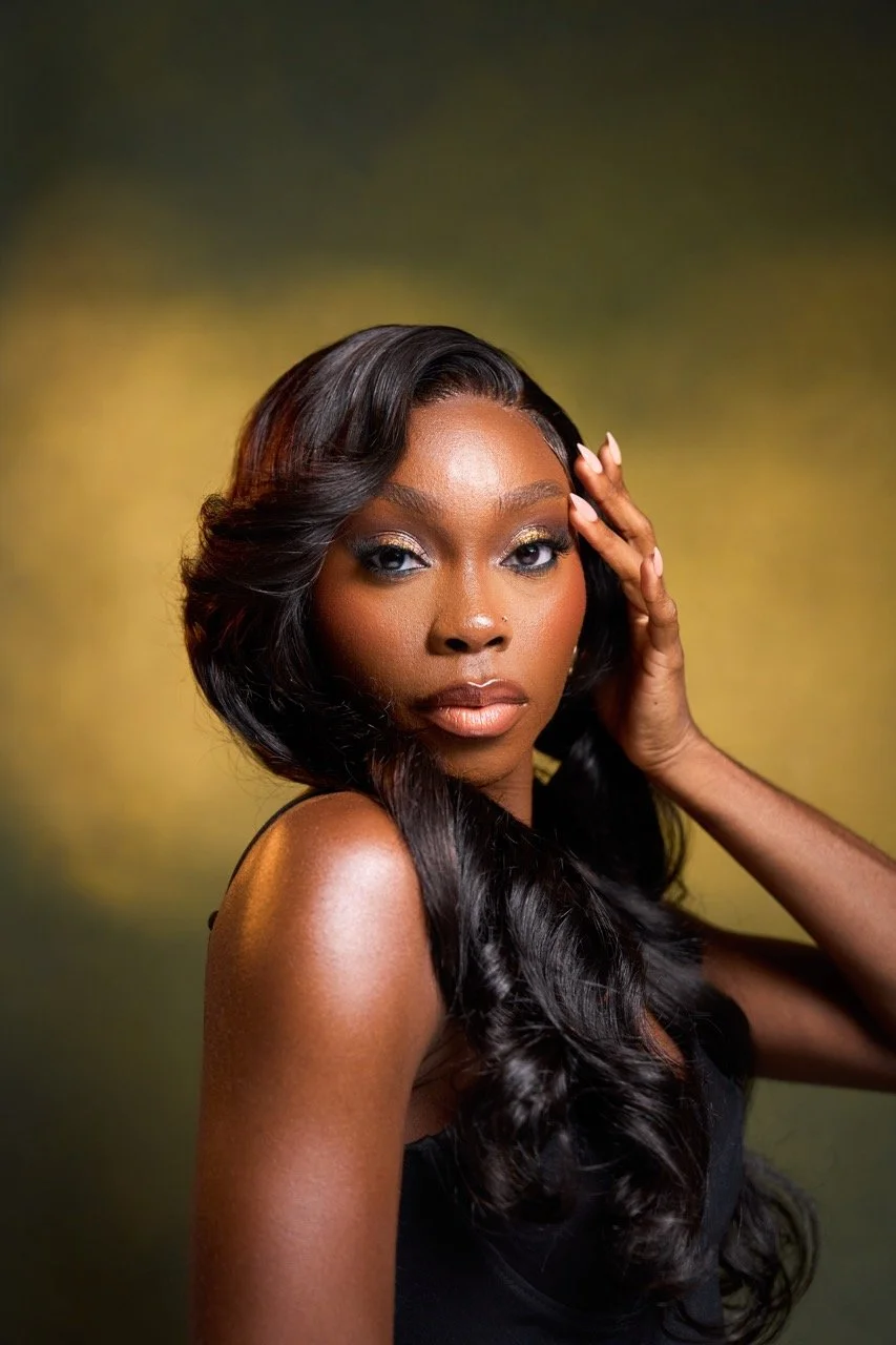 A portrait of a woman with dark, wavy hair, wearing a black sleeveless top, with a golden background.
