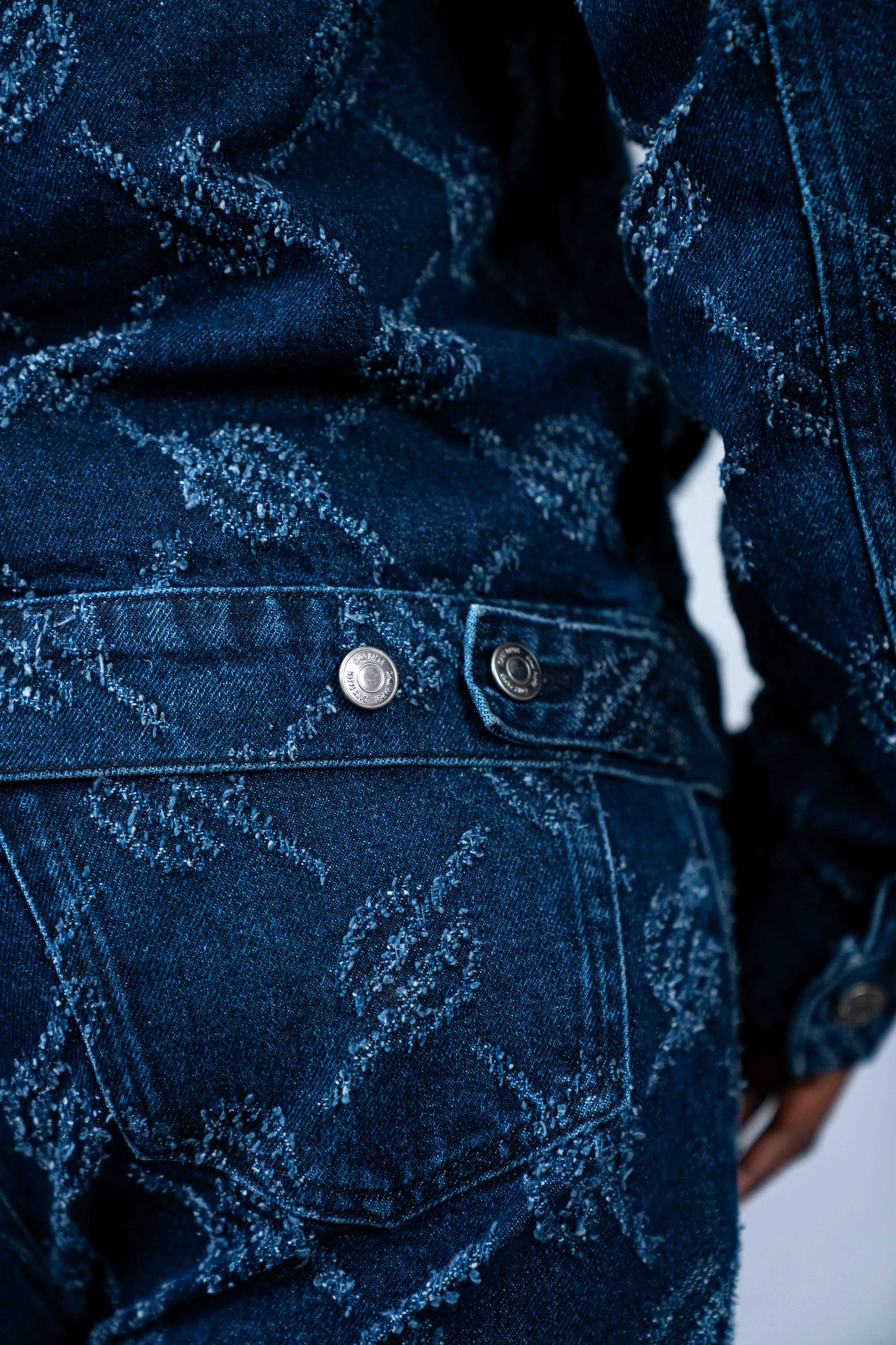 Close-up of a person wearing a dark blue denim jacket and jeans with embroidered design and metal buttons.