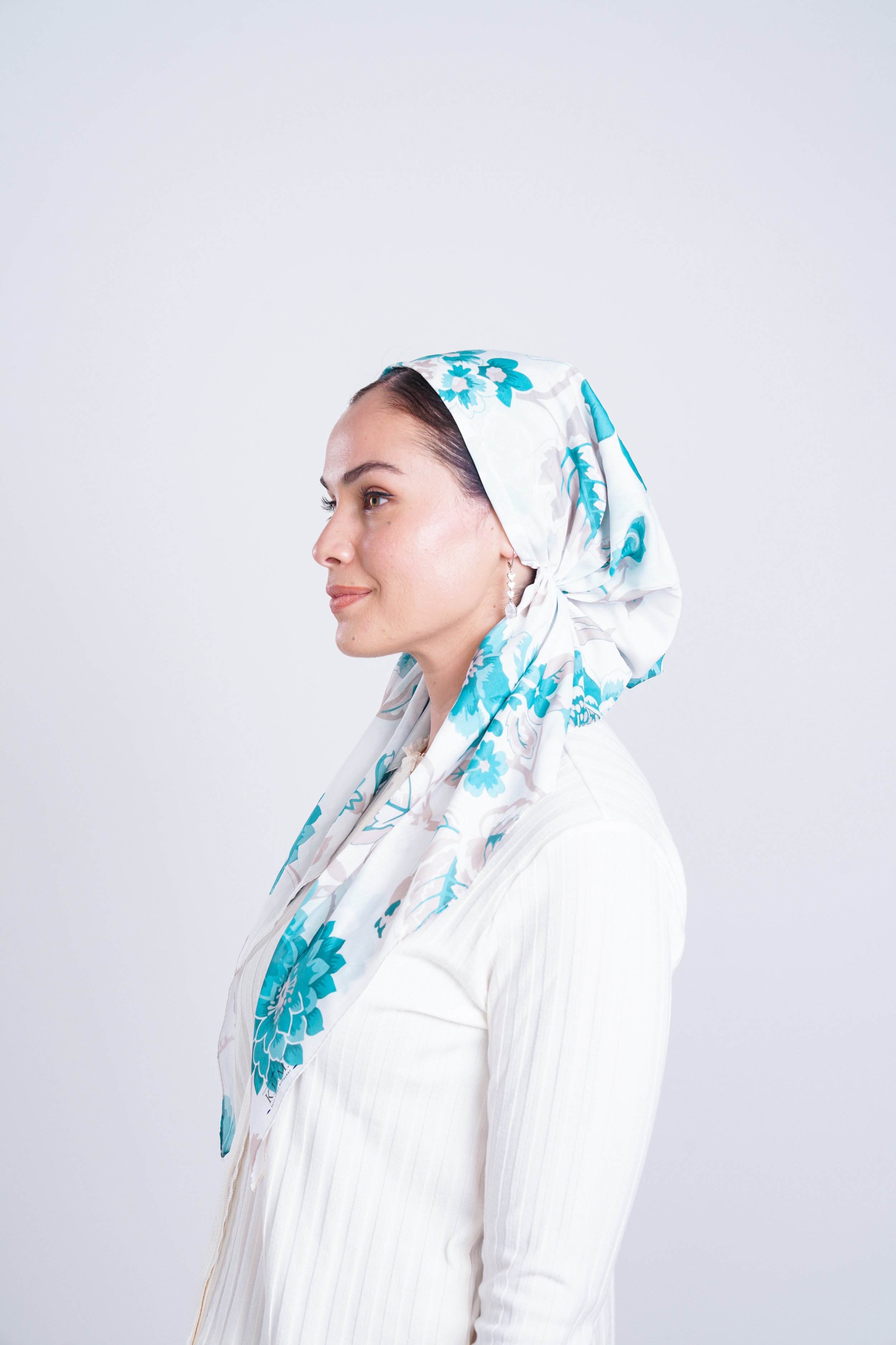 Side profile of a woman wearing a white top and a floral headscarf with blue and white patterns.