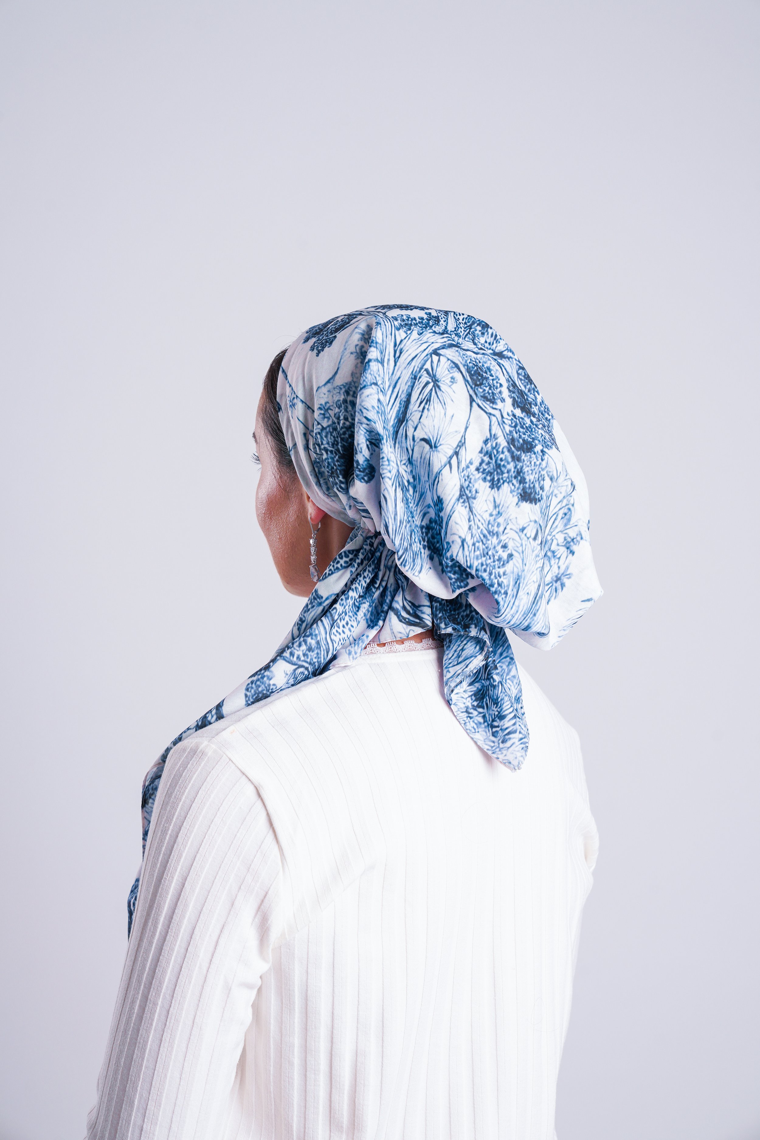A woman facing sideways wearing a white blazer and a blue and white patterned headscarf.