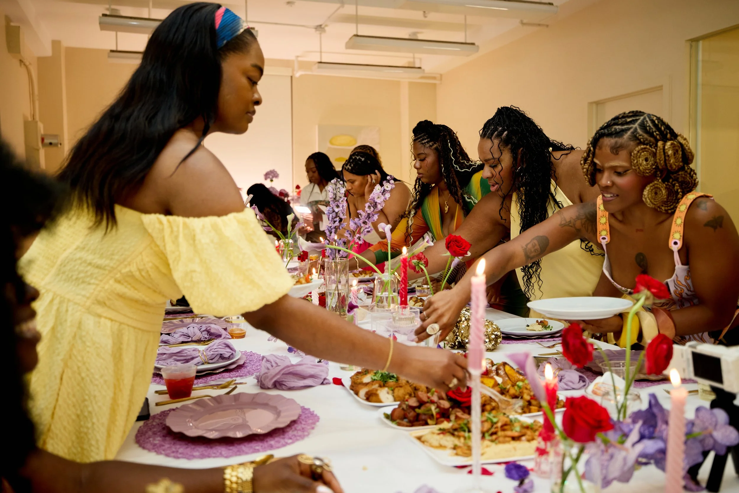 Women gathered around a decorated dining table with food, candles, and flowers, participating in a celebration or gathering.
