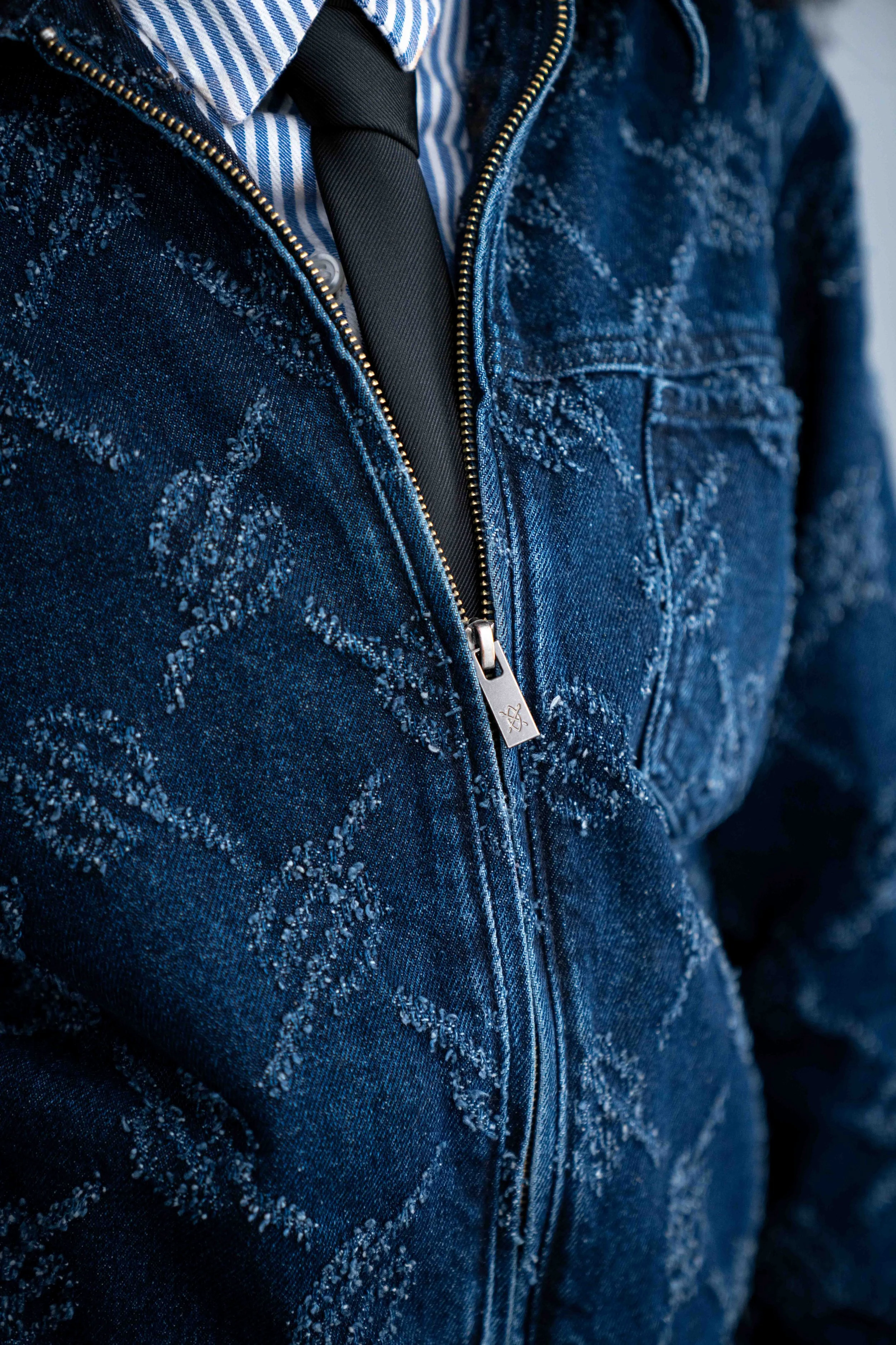 Close-up of a person wearing a distressed denim jacket with star patterns, a striped shirt, a black tie, and a zipper.