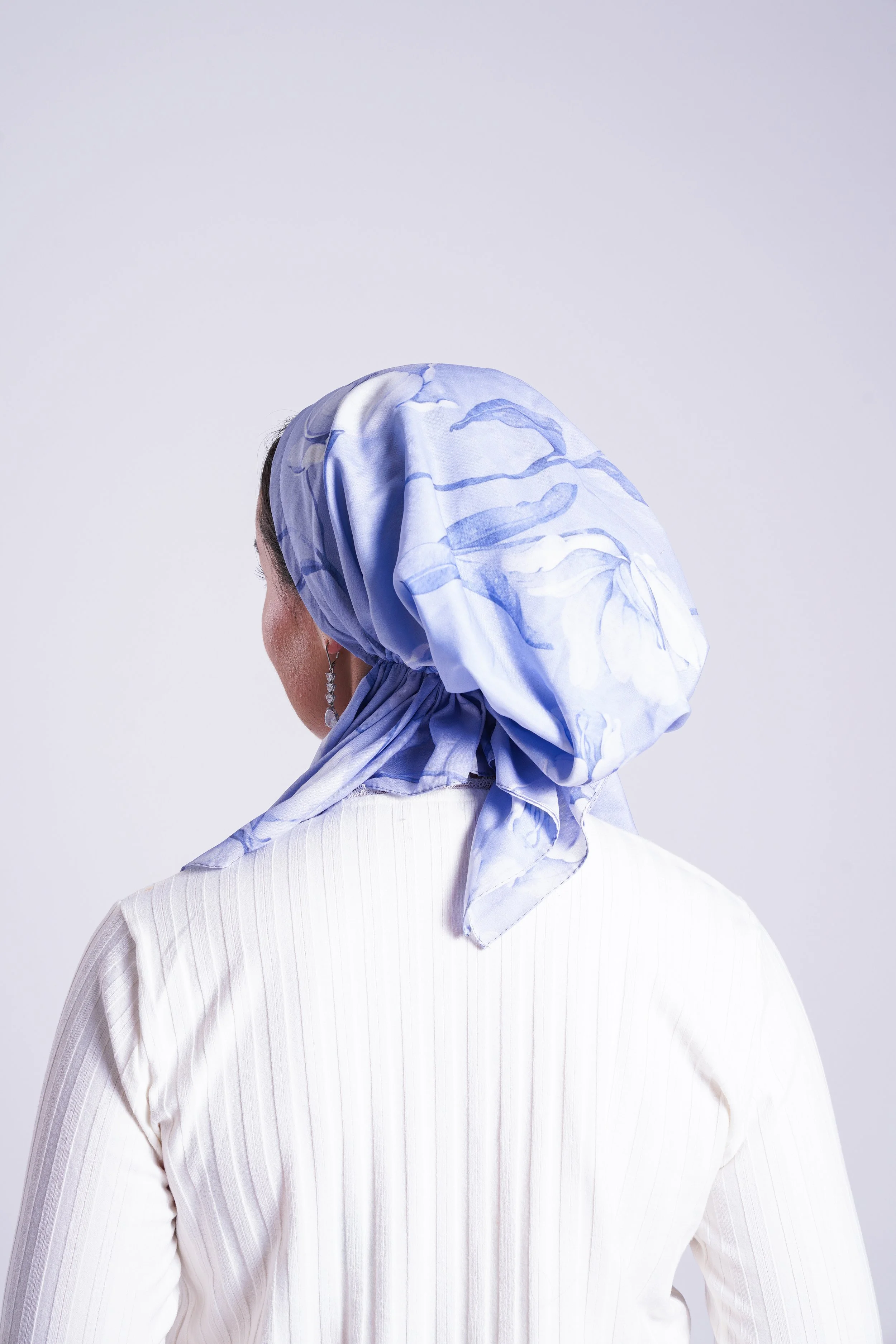 Back view of a woman wearing a blue and white patterned headscarf and white top.