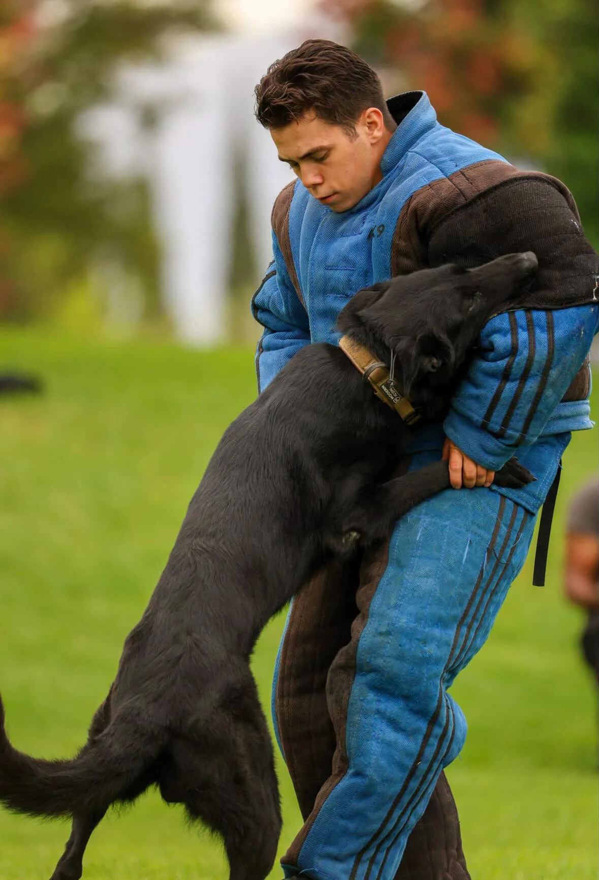 A young man wearing a baseball cap and a hoodie standing outdoors at night, looking serious, with the front legs of a dog or similar animal visible in the foreground.