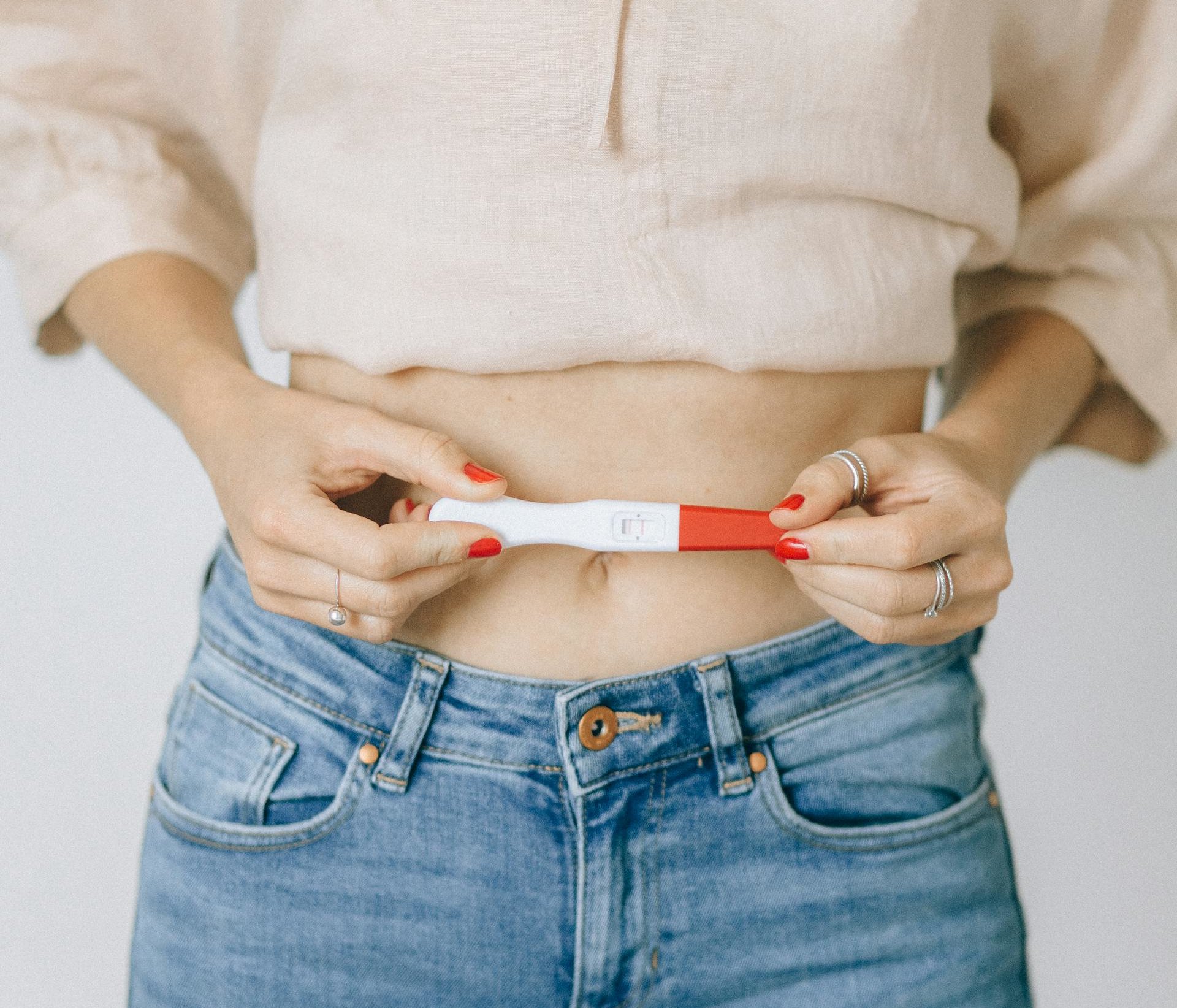 Person holding a pregnancy test near their abdomen after fertility treatments.