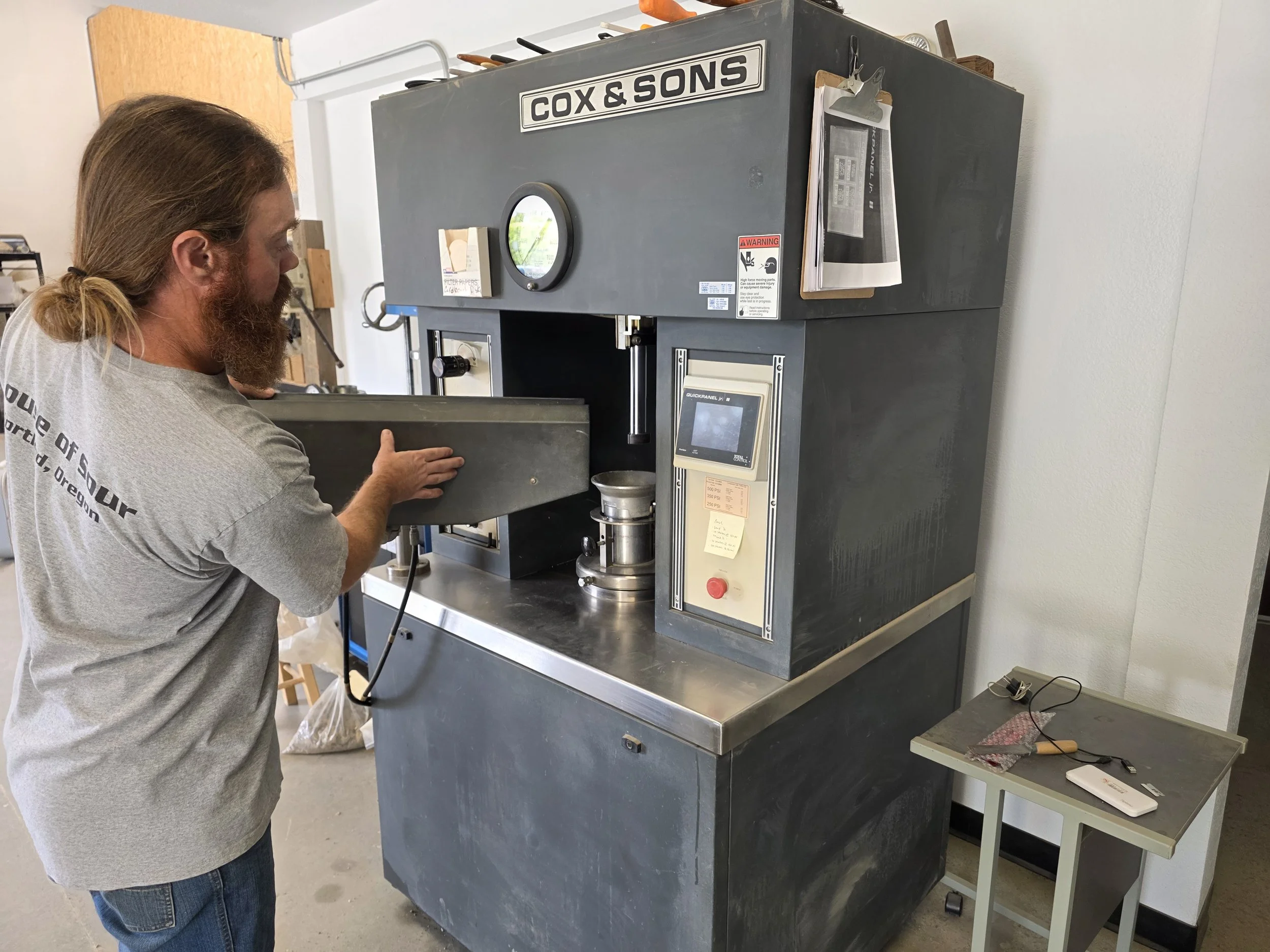 A man operating scientific equipment in a laboratory, using a control panel on a blue device, with various experimental tools and materials on the workbench.