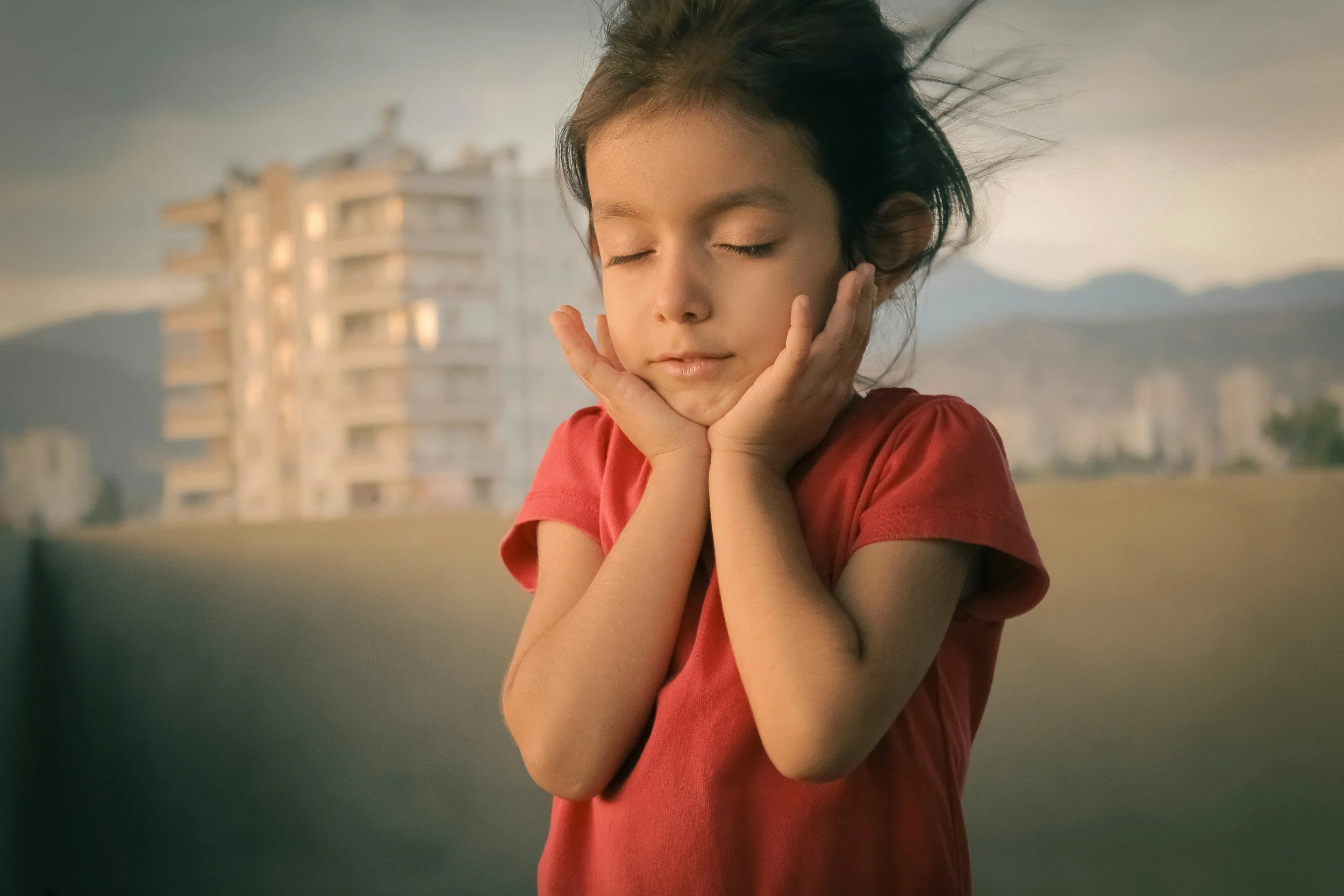 Girl with eyes closed holds her chin with both hands, representing childhood struggle.