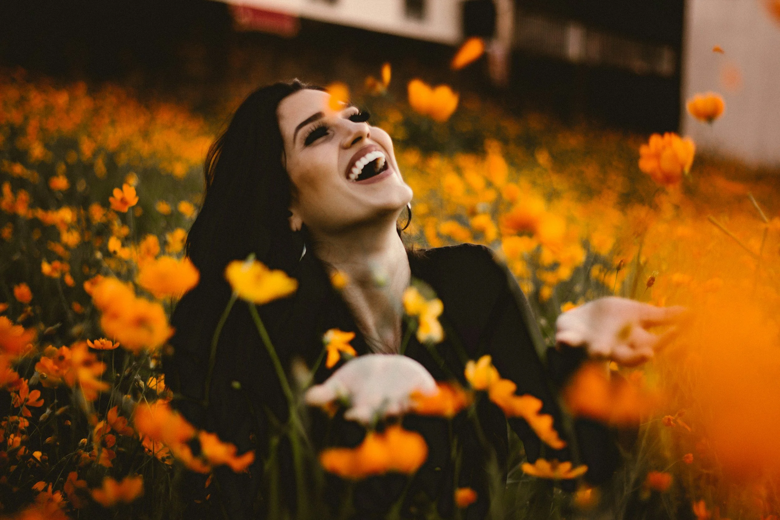 Woman laughing among orange flowers, experiencing joy as an adult.
