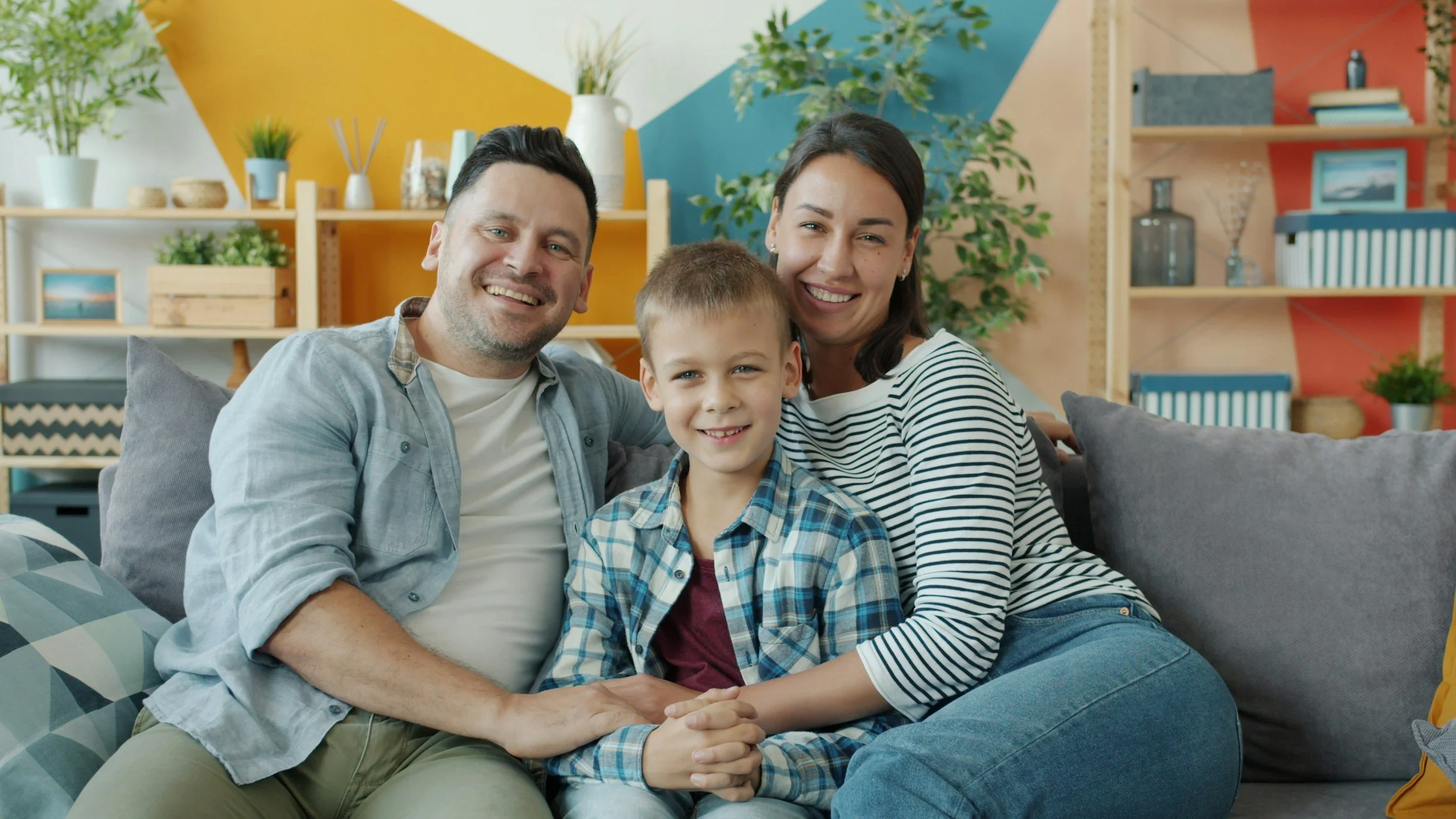 Smiling parents on either side of happy child, sitting on living room couch together.
