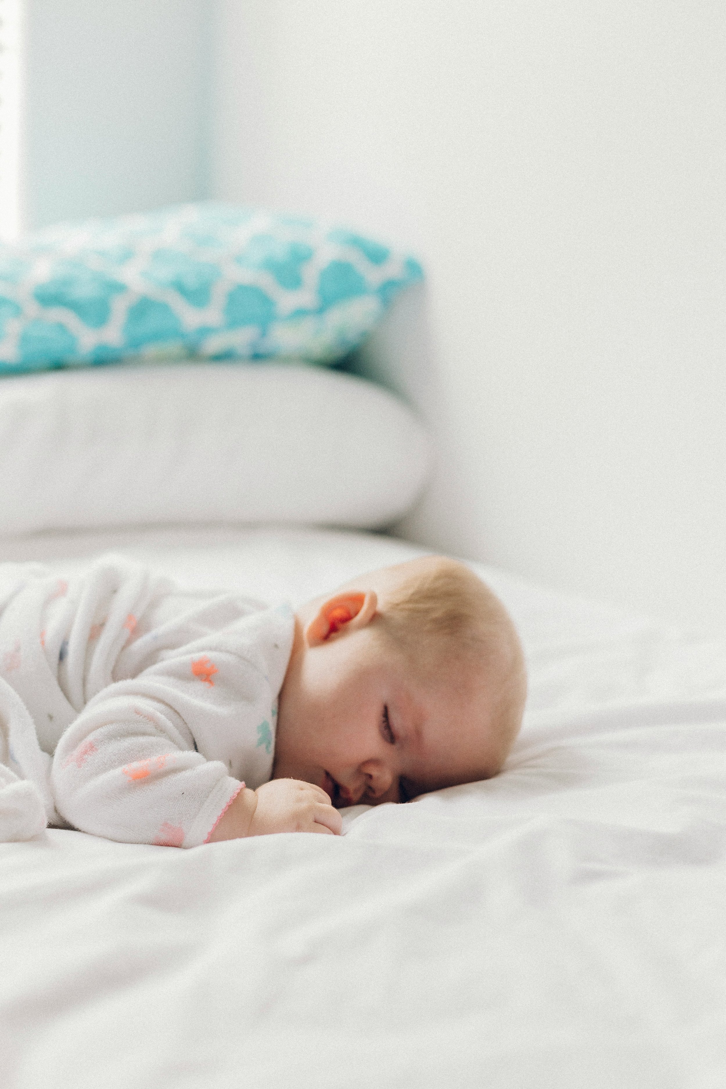 Baby sleeping on a bed with white sheets after sleep consulting services.
