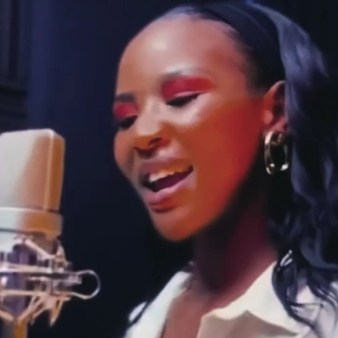 Lucinia Karrey singing into a microphone with a smile, wearing earrings and makeup, in a recording studio.