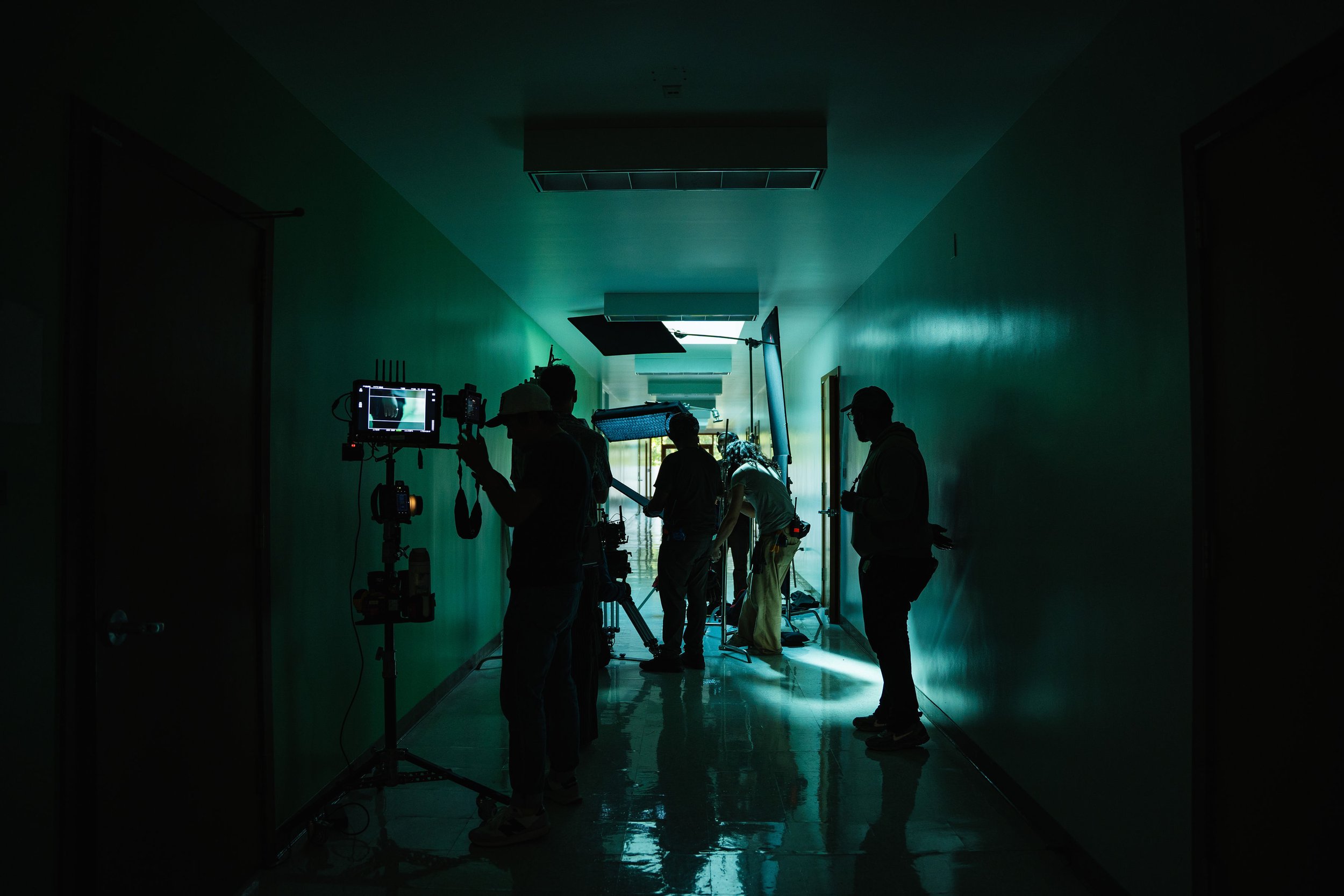 Film production crew working in a dimly lit hallway with equipment and lighting setup.