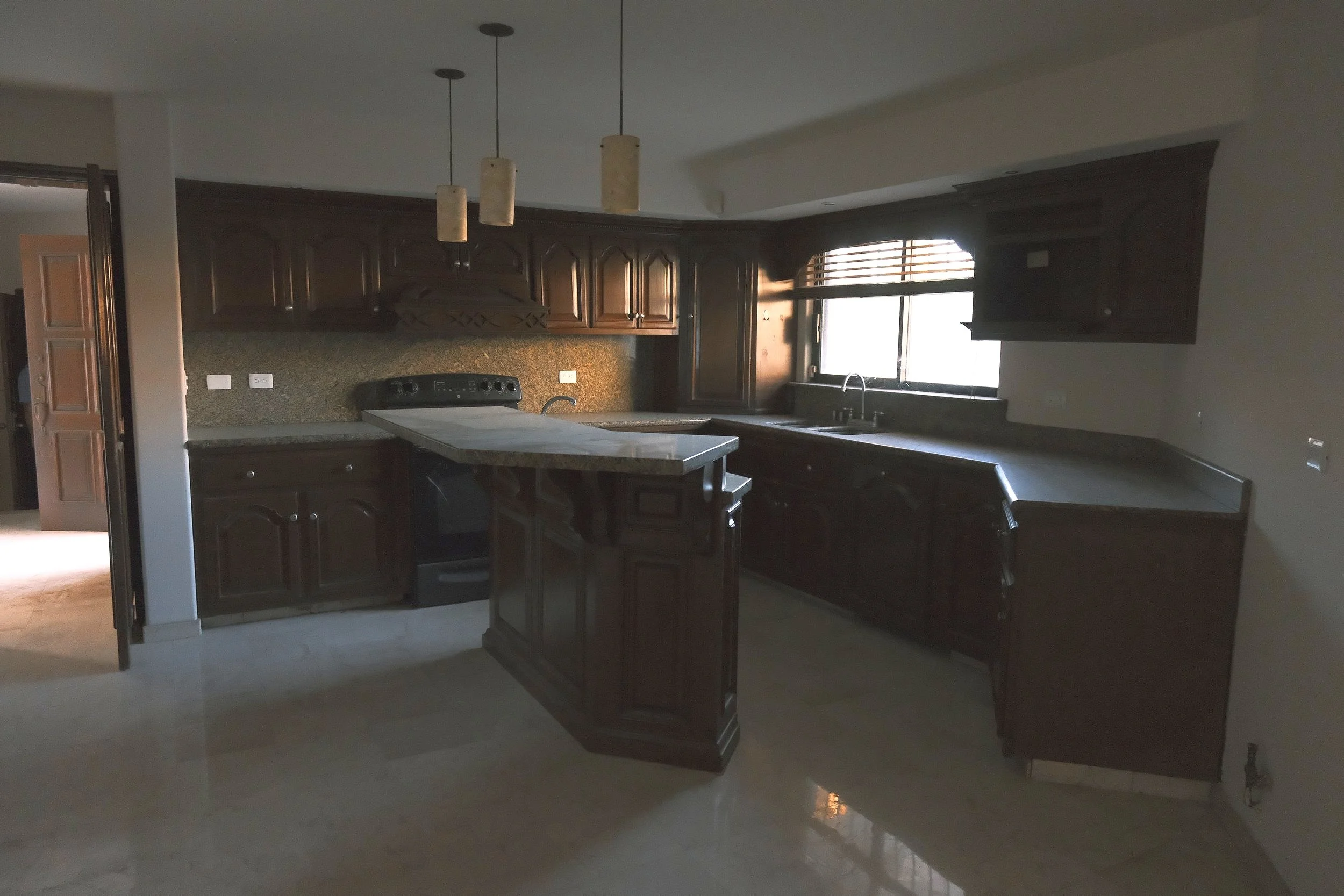 Cocina con gabinetes de madera oscura, encimera de granito y ventana con persianas de madera.