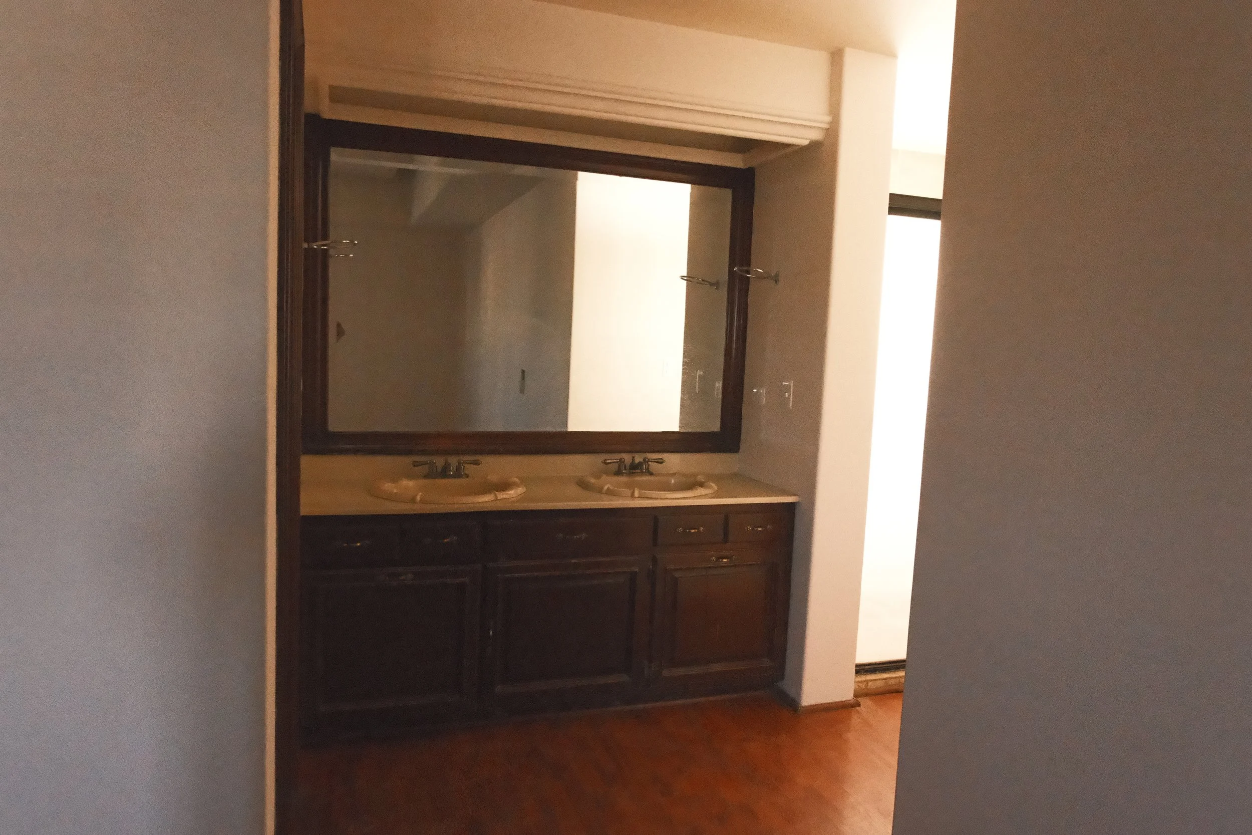 Doble lavabo con un espejo grande, encimera de piedra y gabinete de madera oscuro en un baño.