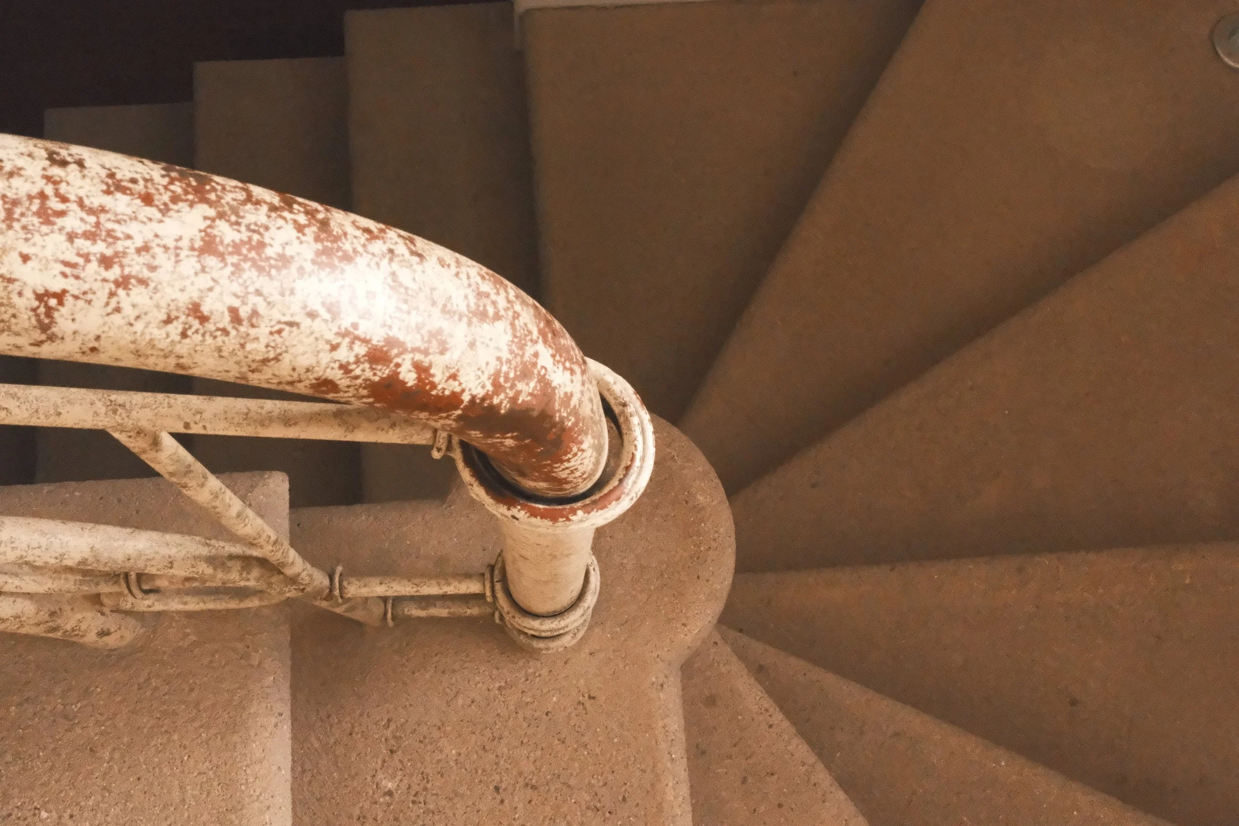 Vista desde arriba de una escalera de SPIRAL con barandilla metálica oxidada.